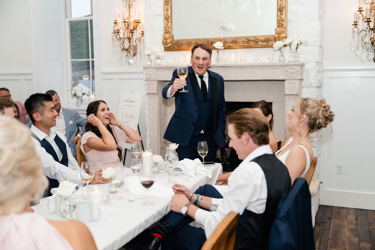 Wedding celebration in an elegant white room with ornate gold mirror and chandelier.