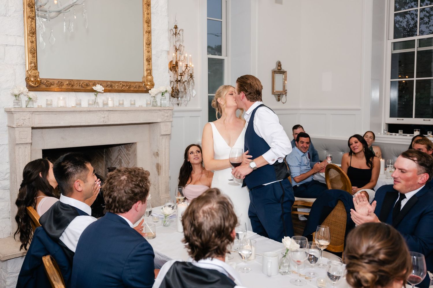 Wedding reception guests enjoying dinner in an elegant white-walled dining room.