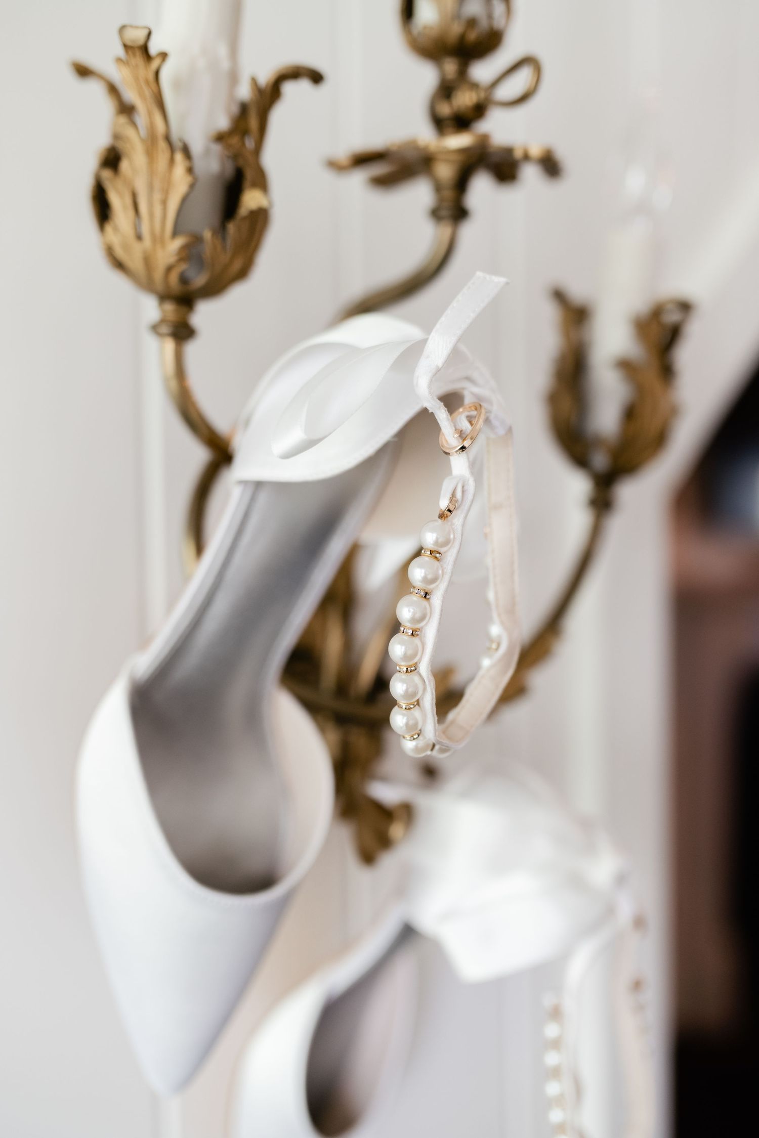 White bridal shoe and crystal headpiece displayed against antique gold wall sconce.