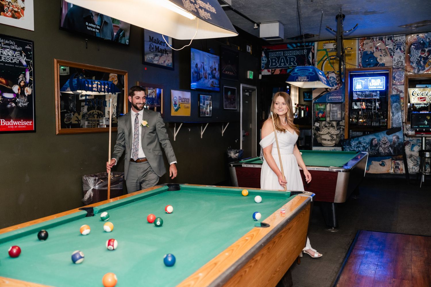 A couple plays pool in a casual bar setting with sports memorabilia on the walls.