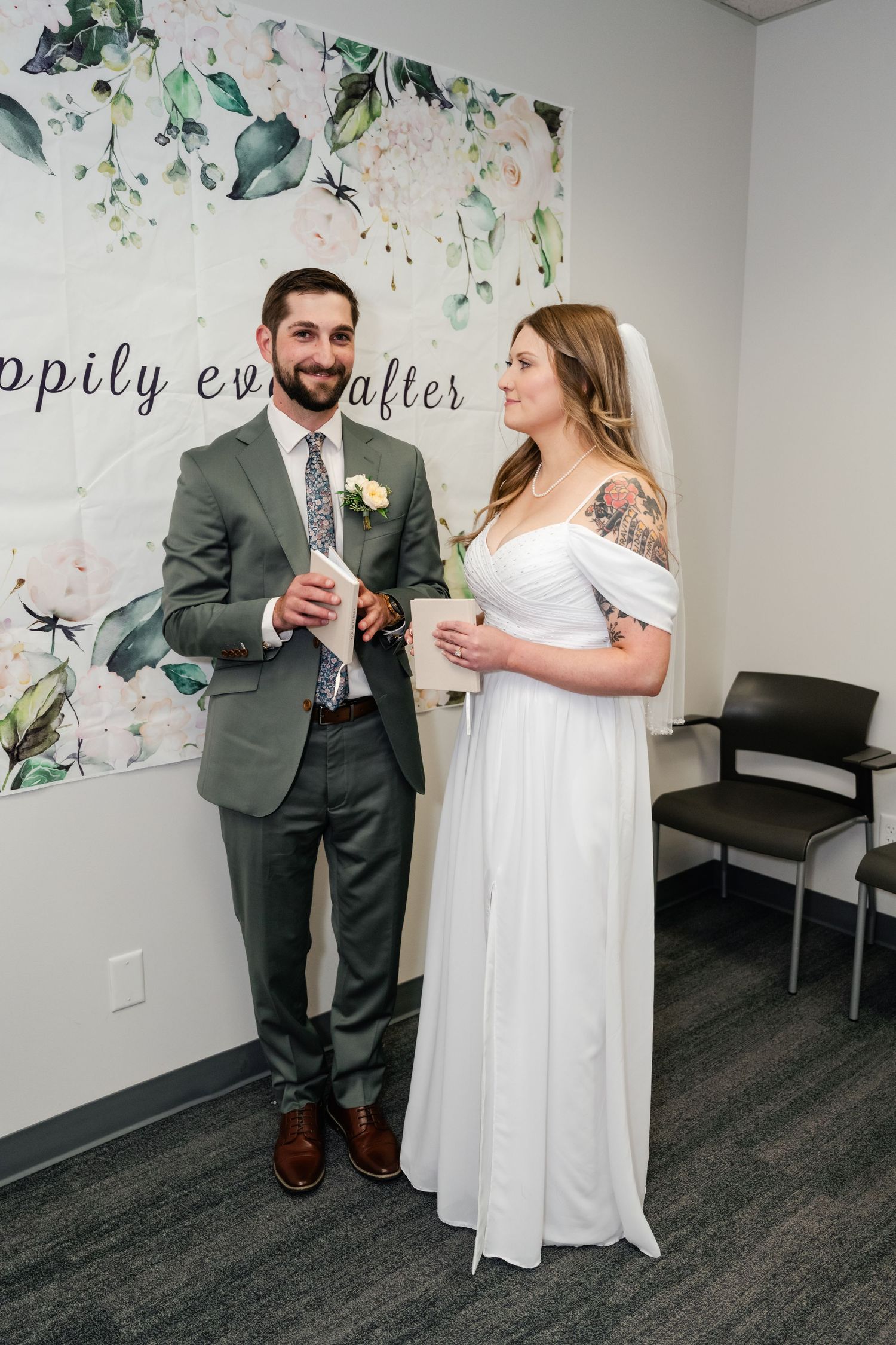 A couple in wedding attire shares a private moment in an office space decorated with floral wall art.