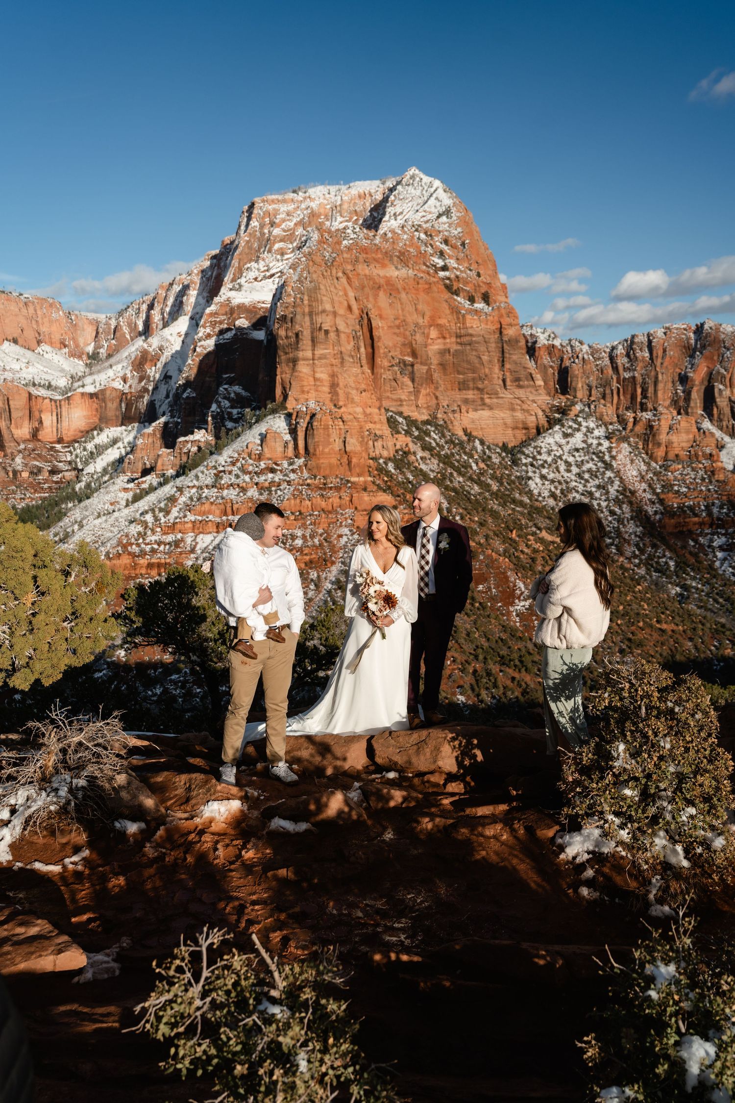 A small wedding ceremony unfolds against majestic snow-capped red rock formations.