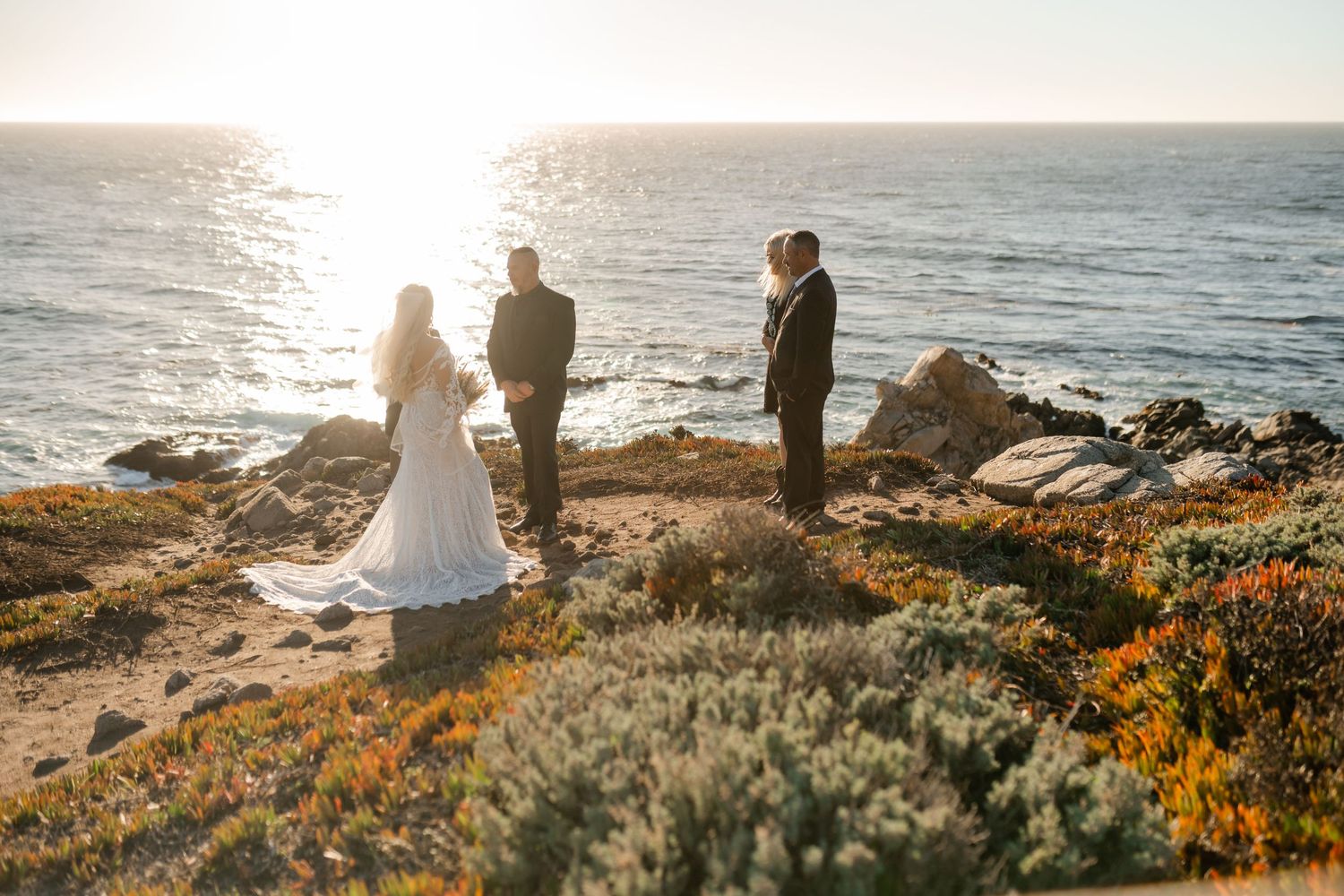 Golden hour wedding photos captured on a dramatic oceanside cliff with wildflowers and natural scenery.