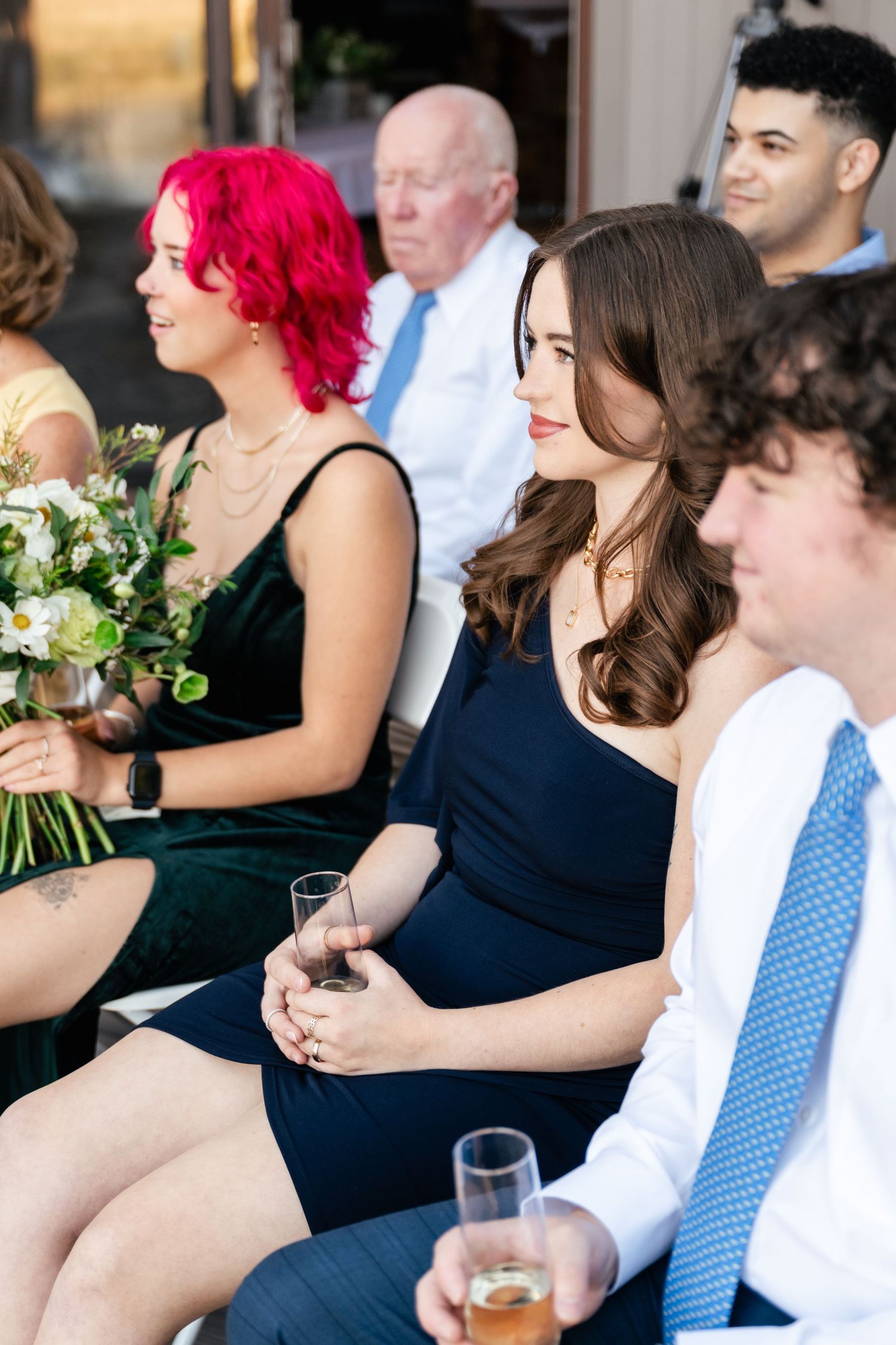 Wedding guests in formal attire seated in rows during an outdoor ceremony.