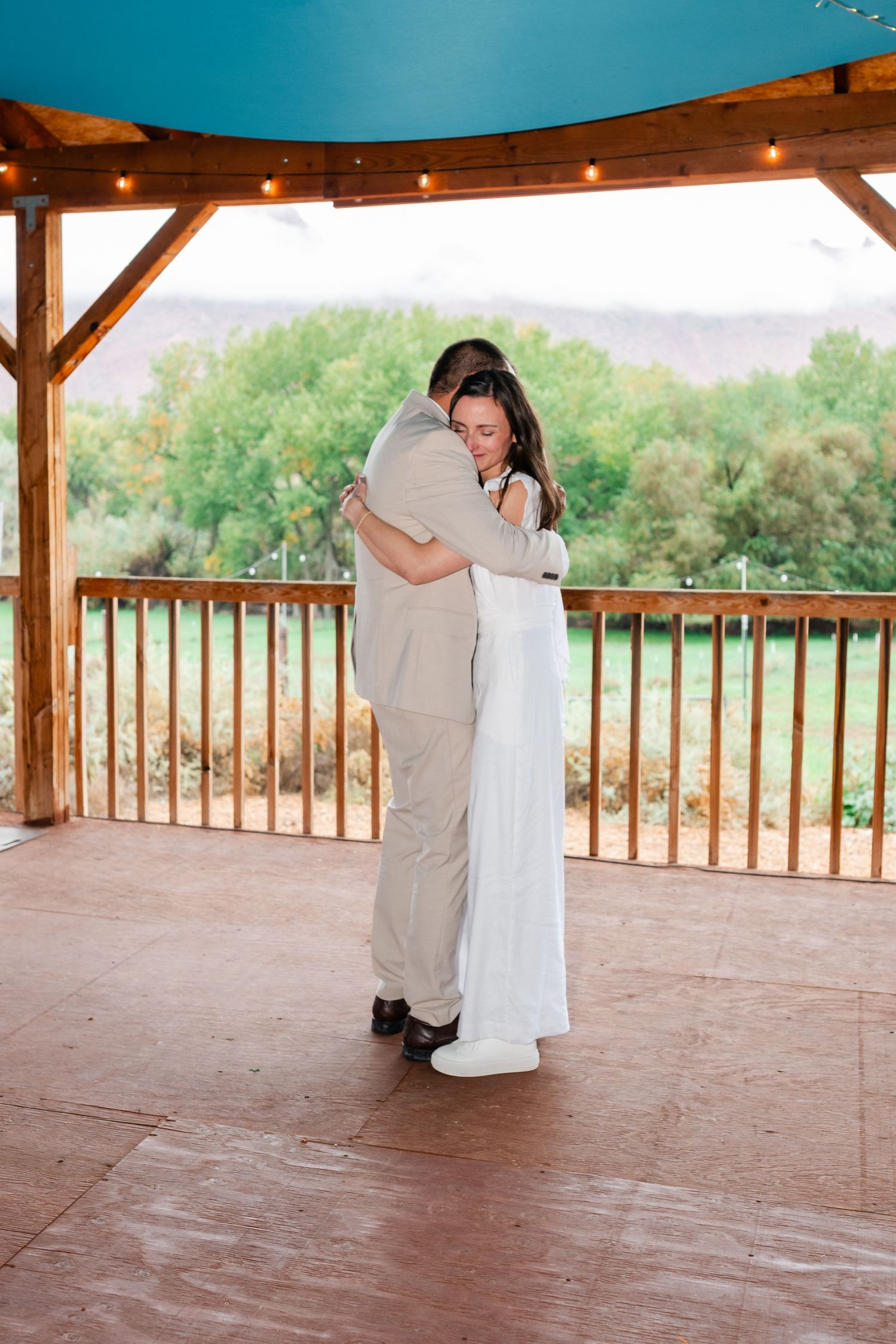 A couple shares a romantic first dance on a covered outdoor patio with mountain views in the background.