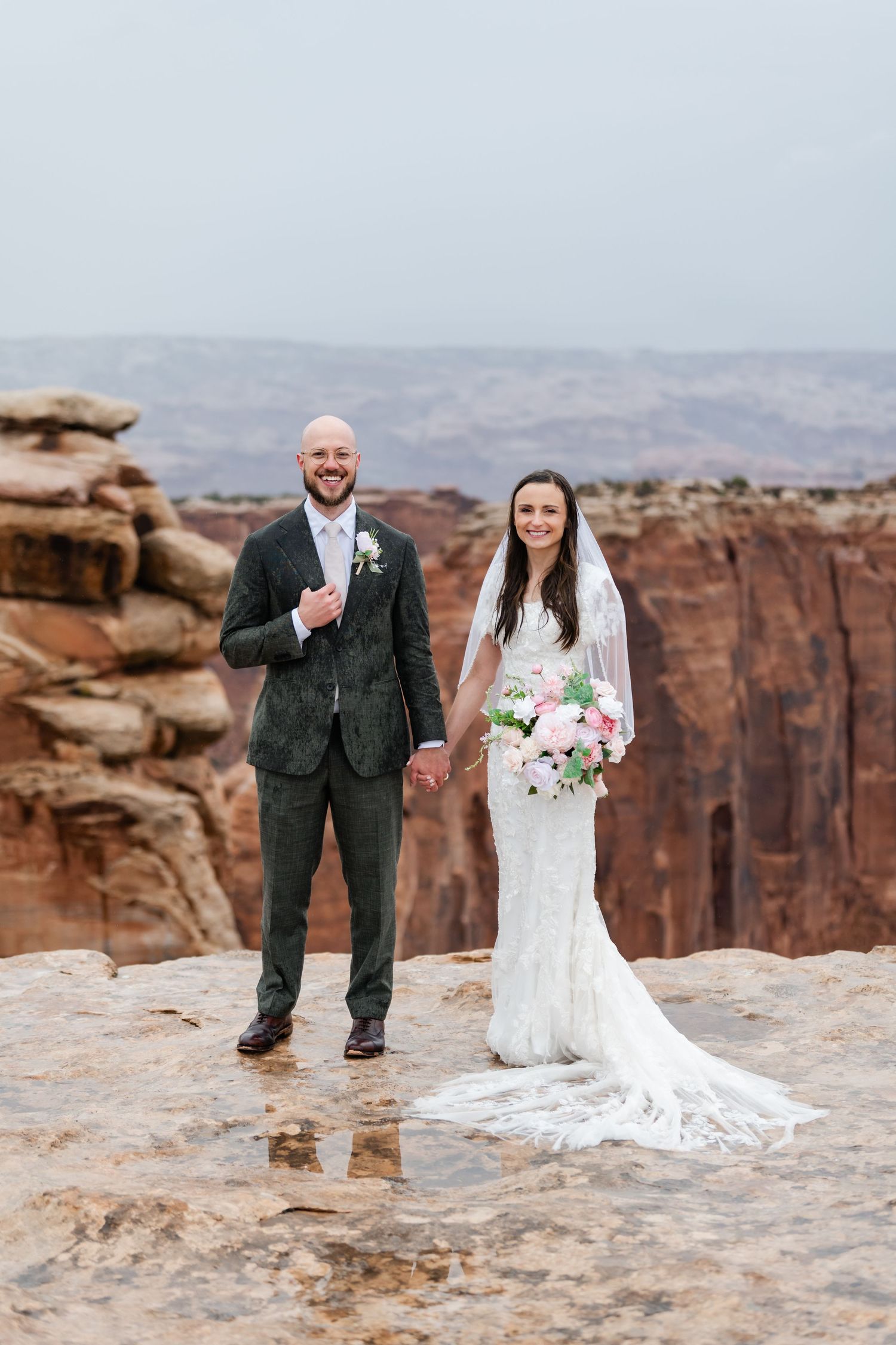 A wedding couple shares a joyful moment on the edge of a vast canyon landscape.