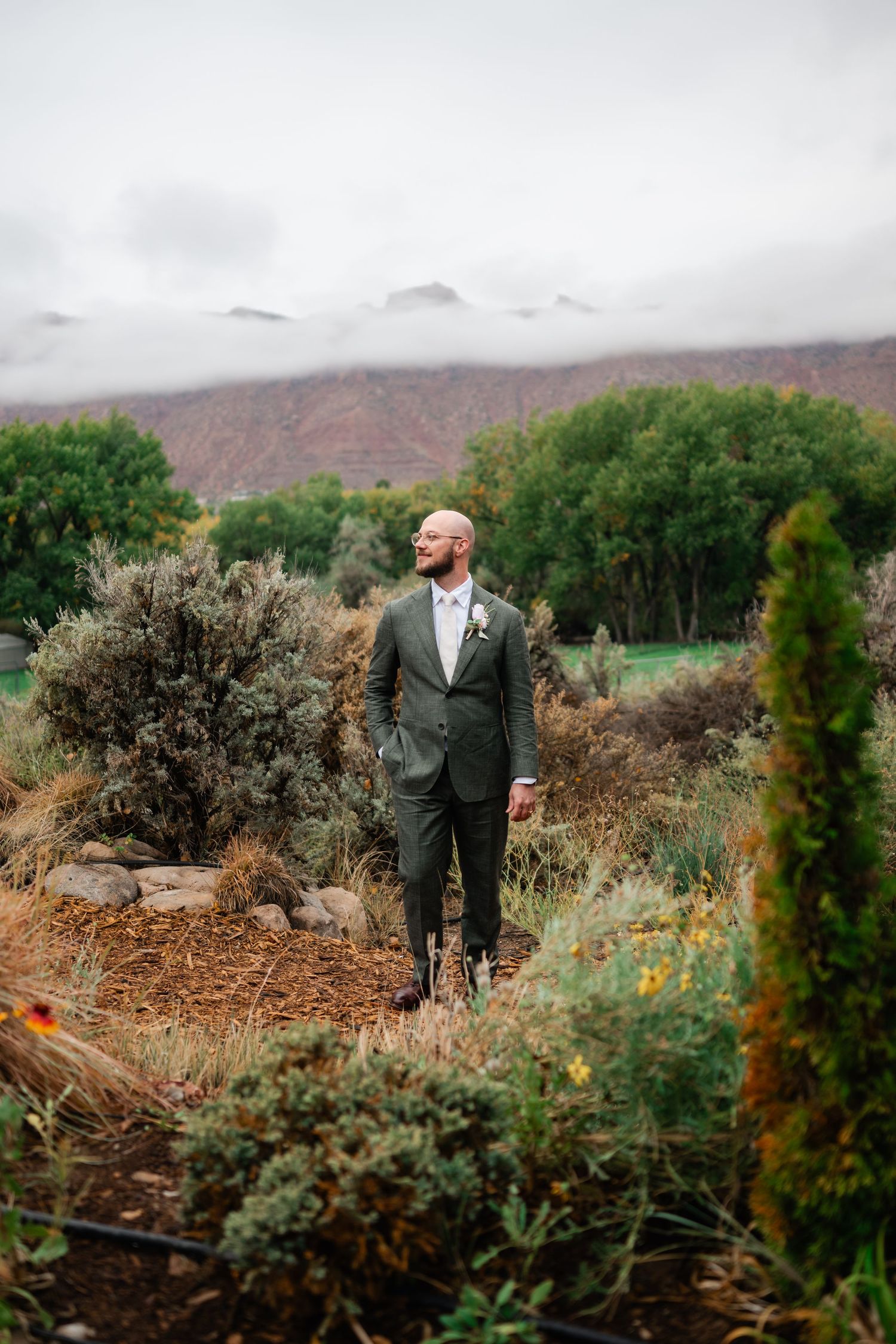 A scenic wedding photo in a desert landscape with mountains and green foliage in the background.
