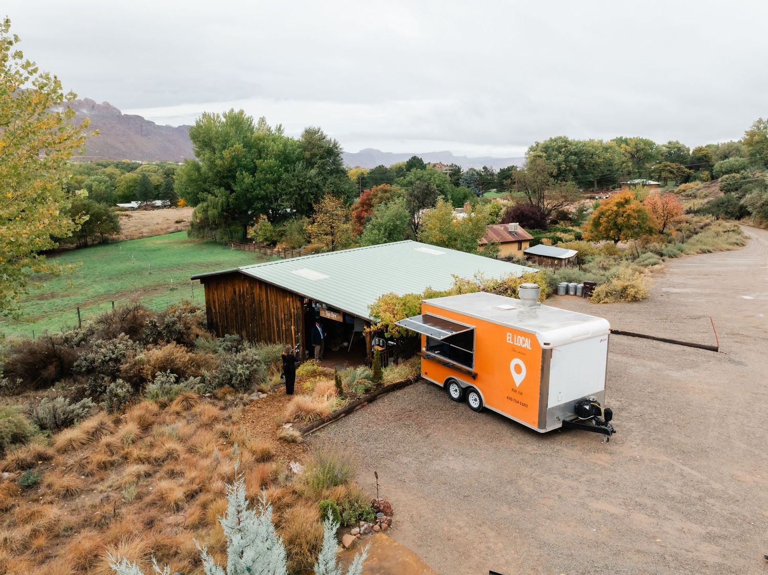 Aerial view of a rustic wooden shelter and food truck parked in a desert landscape with mountains in the background.