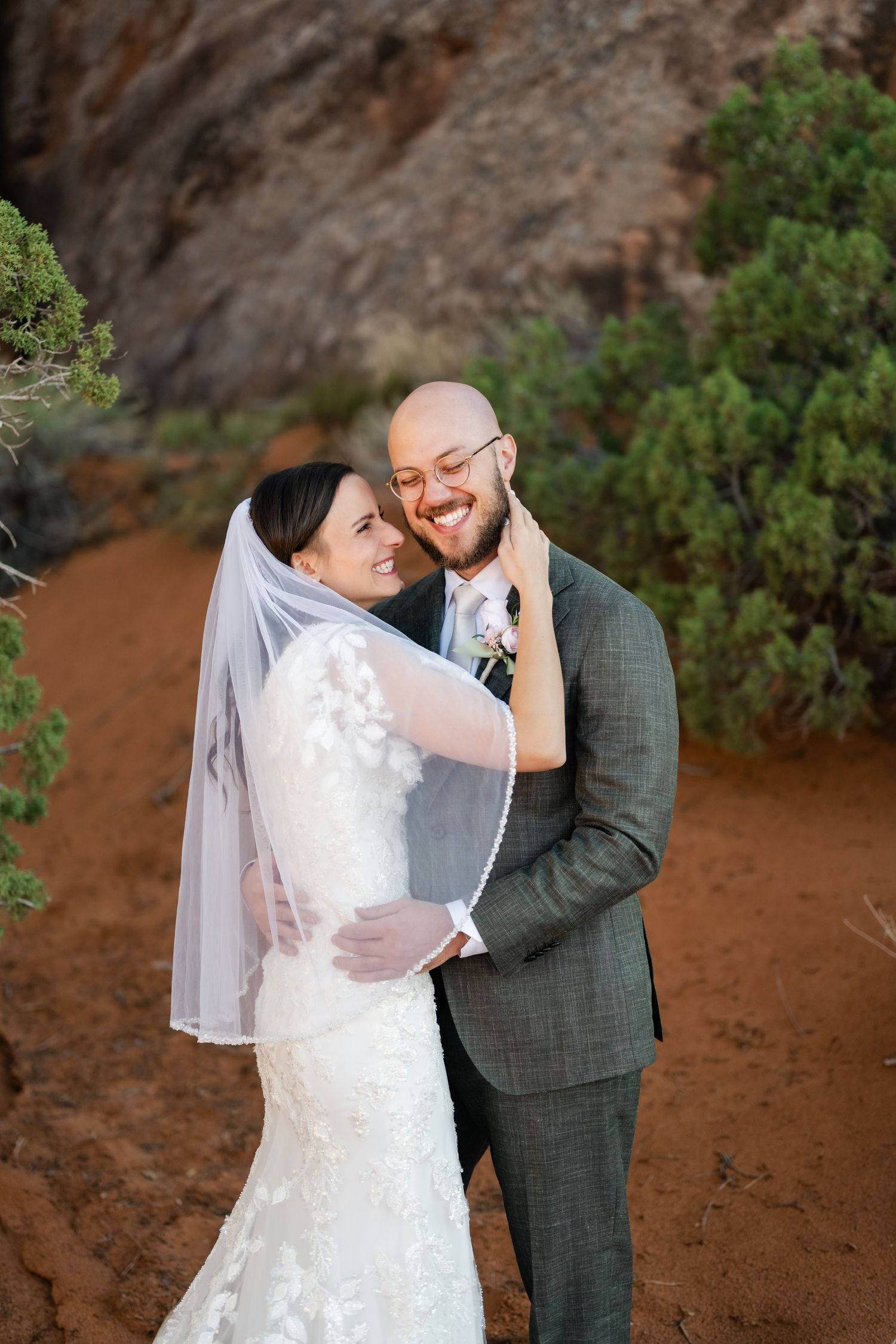 A romantic wedding portrait captured against rustic desert cliffs and vegetation.