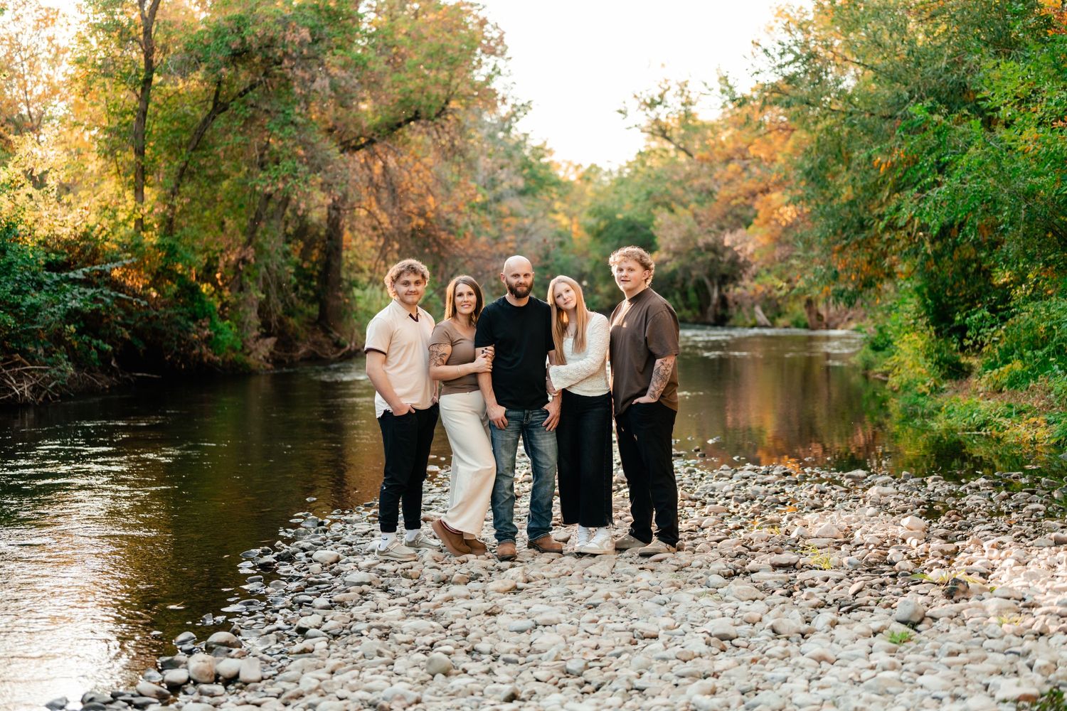 A group stands together on a rocky riverbank surrounded by autumn foliage and reflecting water.