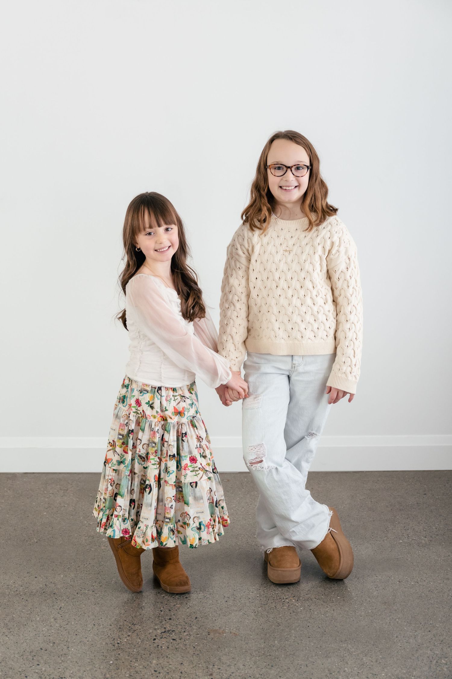 Two people in casual outfits pose together showing their shoes and legs against a white studio background.