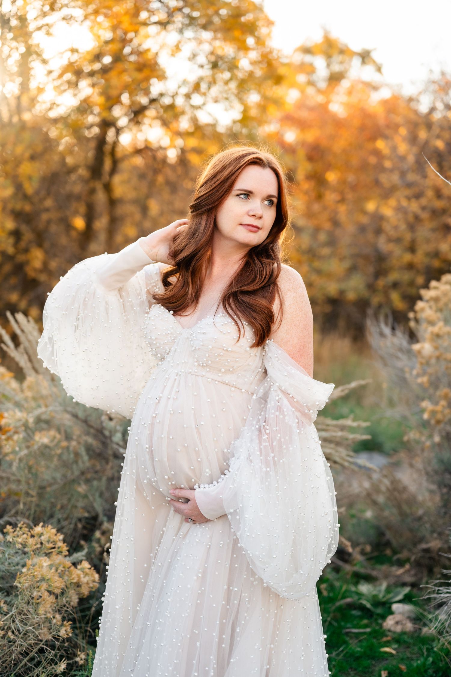 A dreamy portrait in a white lace dress against golden autumn foliage during sunset in a natural outdoor setting.