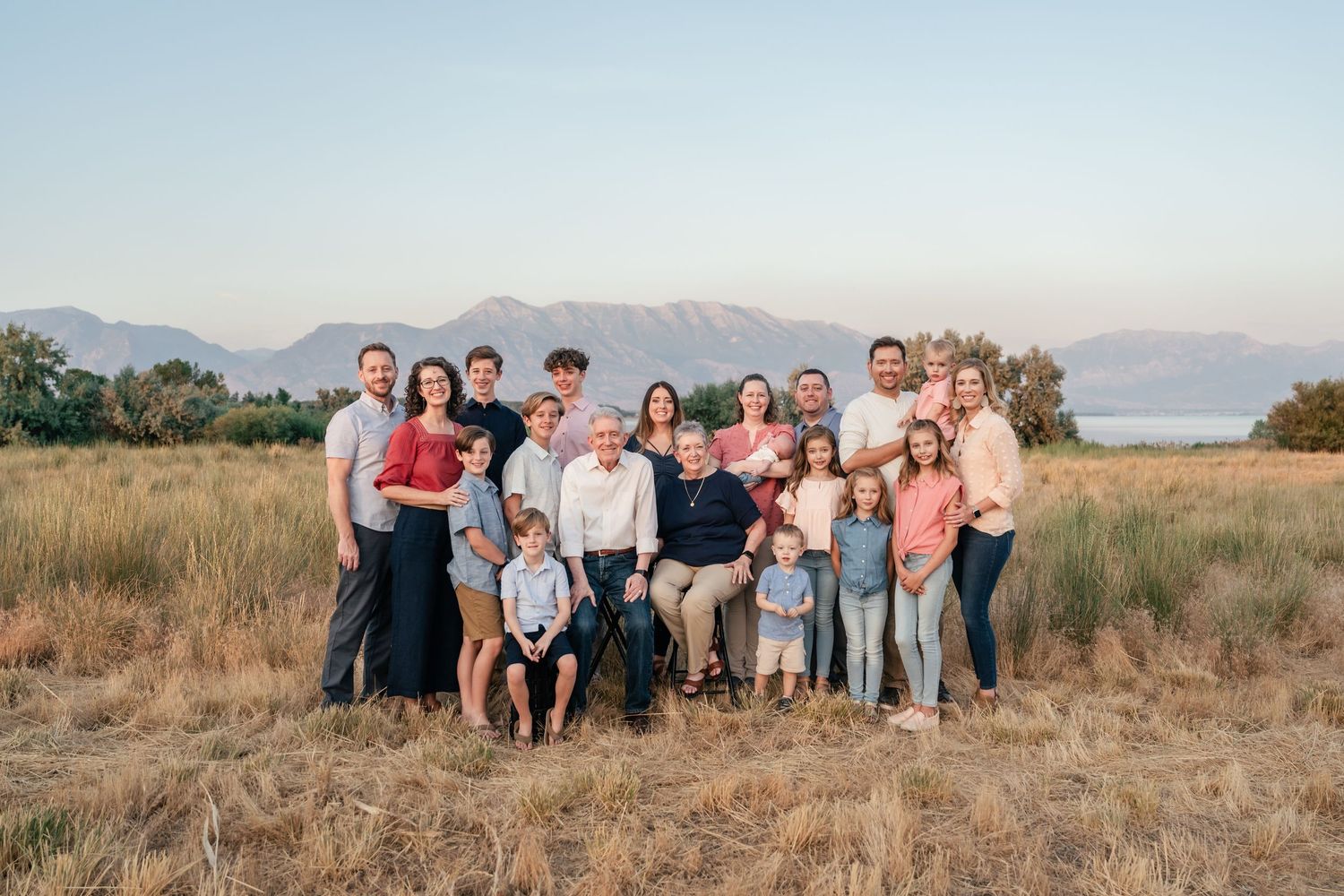 A group of people sitting and standing together in casual attire on a grassy hillside during sunset.