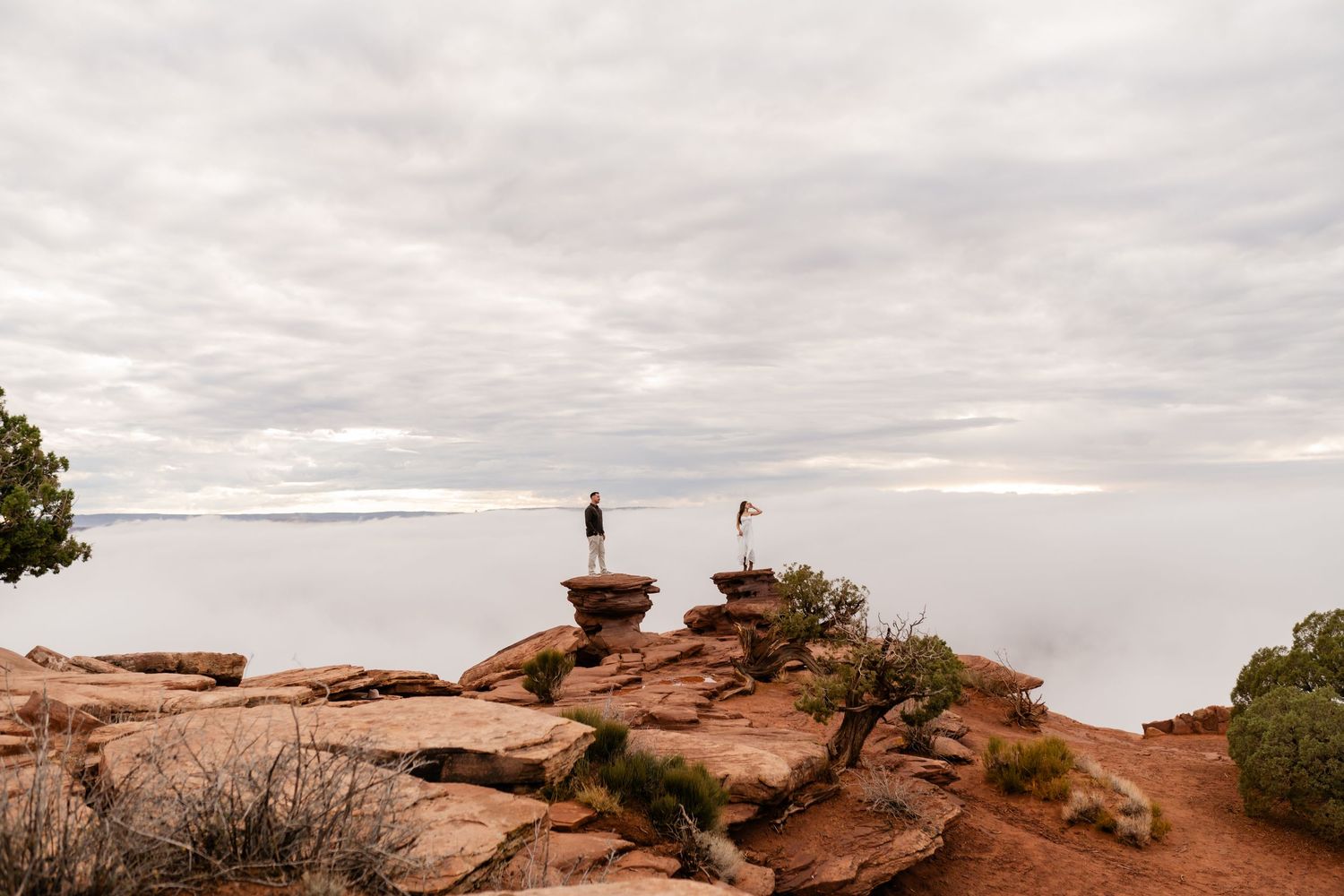 A silhouetted figure stands on red rock formations at Arches National Park during sunset against a cloudy sky.