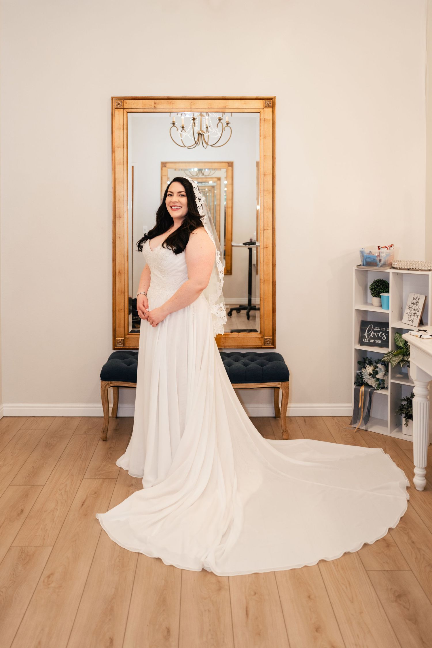 Elegant bridal gown with flowing train displayed in a boutique setting with wooden framed mirror.