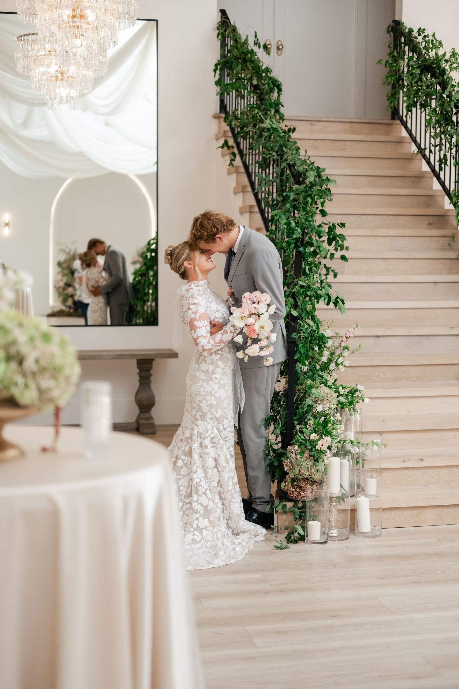 Elegant wedding scene with lace dress and greenery-adorned staircase in a luxurious indoor venue with crystal chandelier. Utah Wedding Photo
