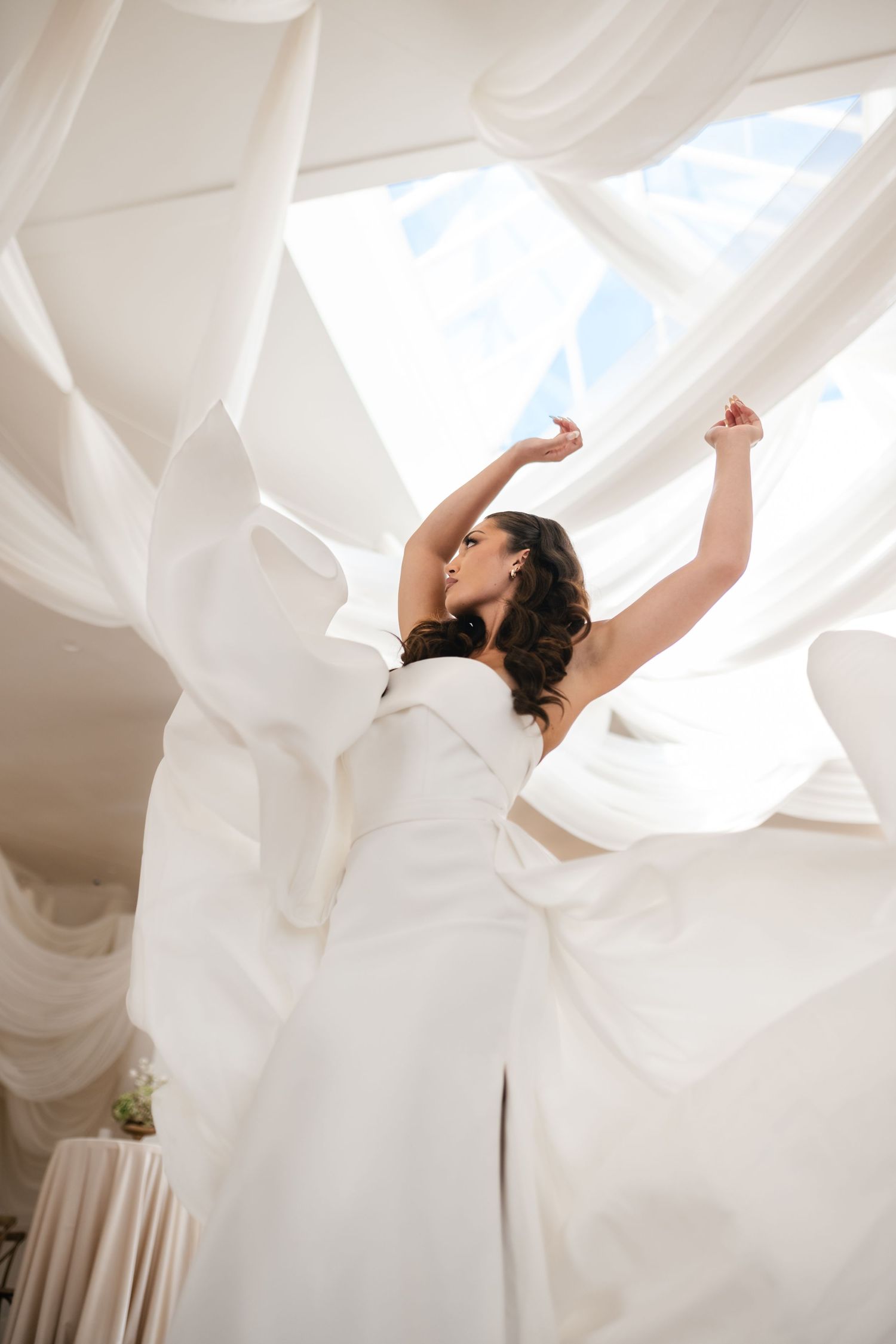 Dancing bride in flowing white dress twirls beneath billowing fabric canopy with natural skylight above. Utah Wedding Photographer.