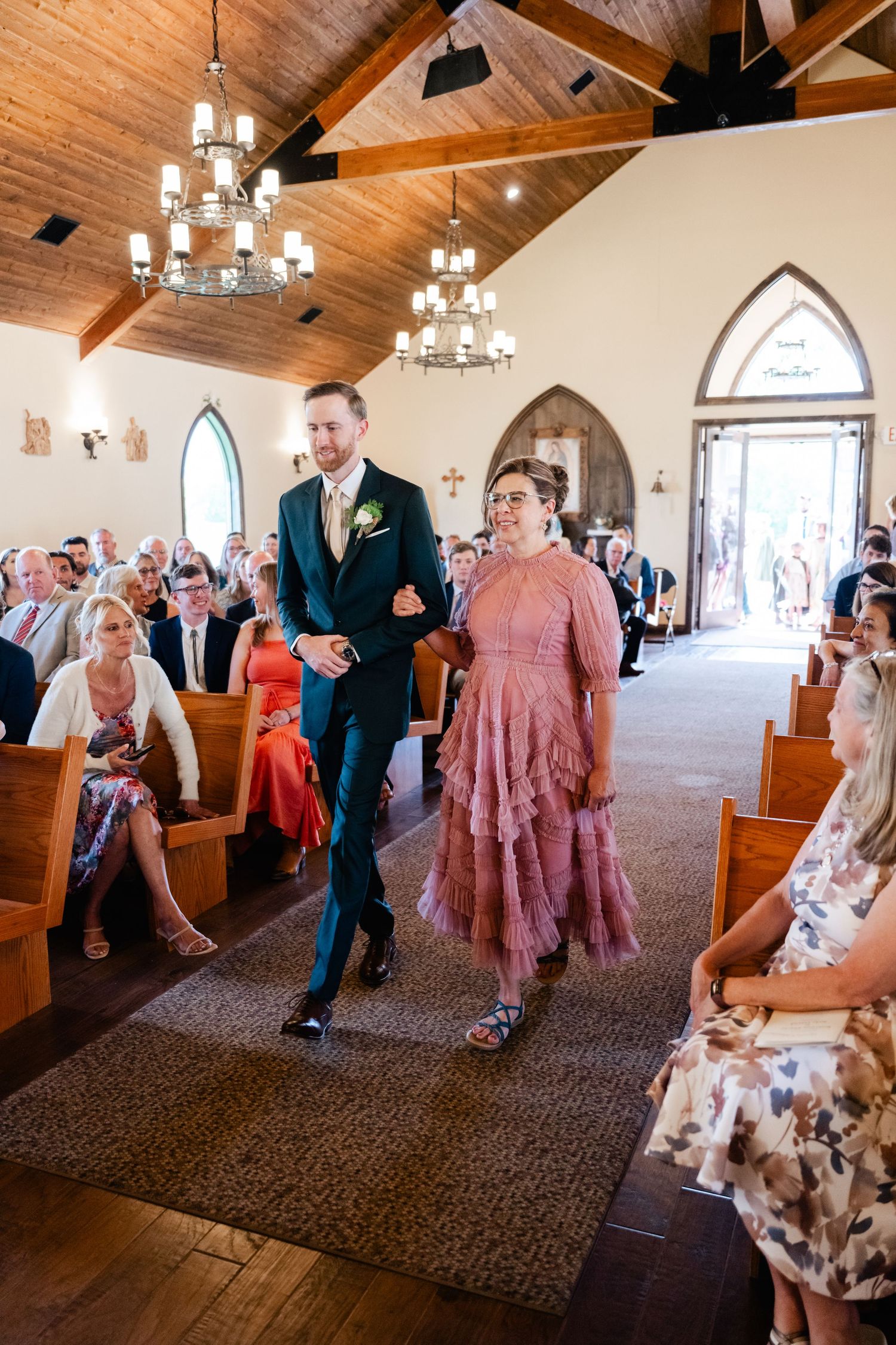 Wedding guests dance and celebrate on the carpeted floor of a church reception hall with wooden beam ceilings.
