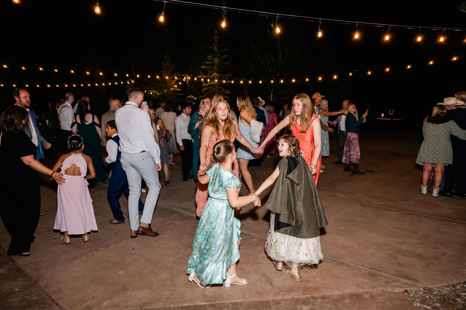 People enjoying an evening celebration under twinkling string lights at an outdoor venue.