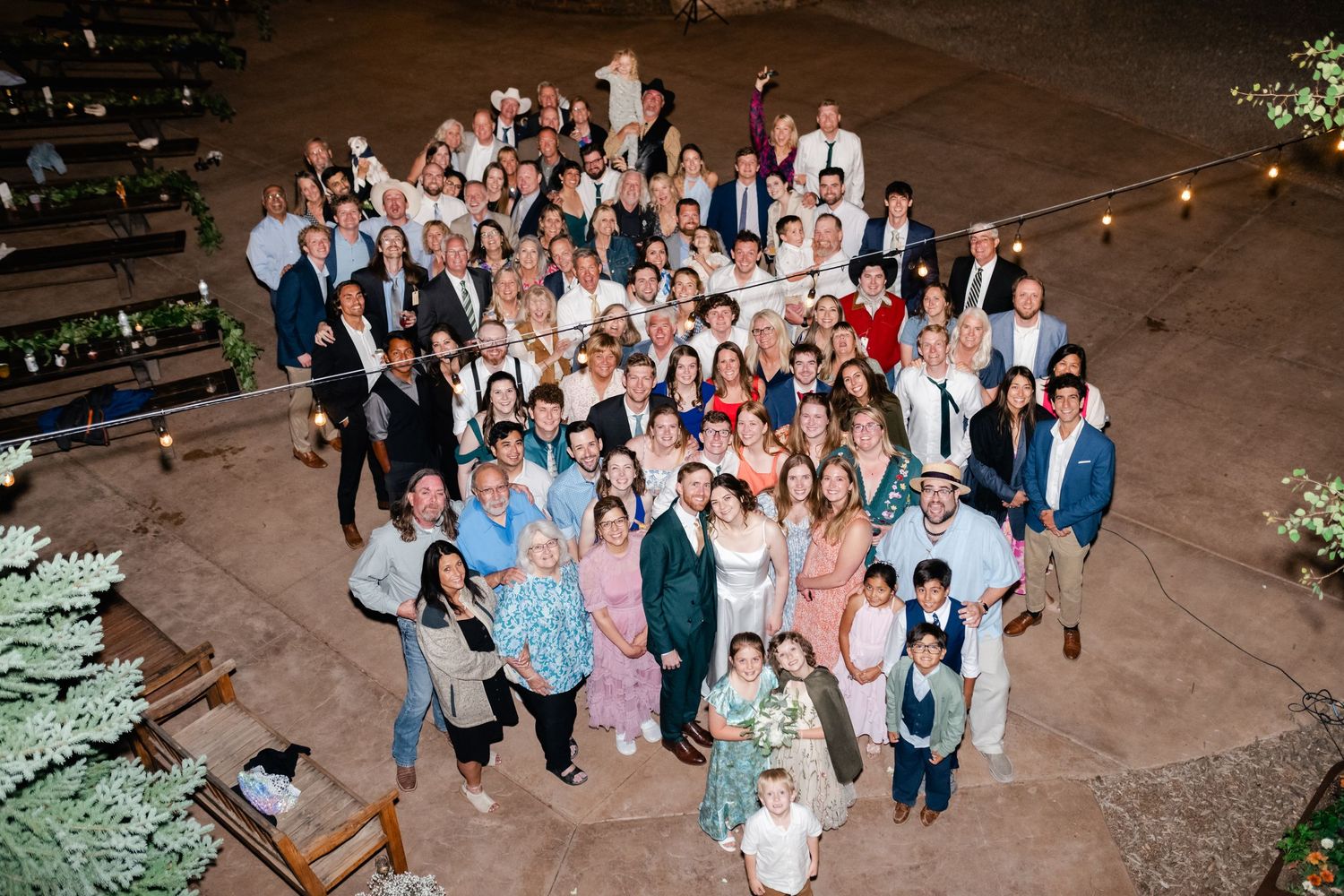 Large group photo of wedding guests gathered on an outdoor patio at night.