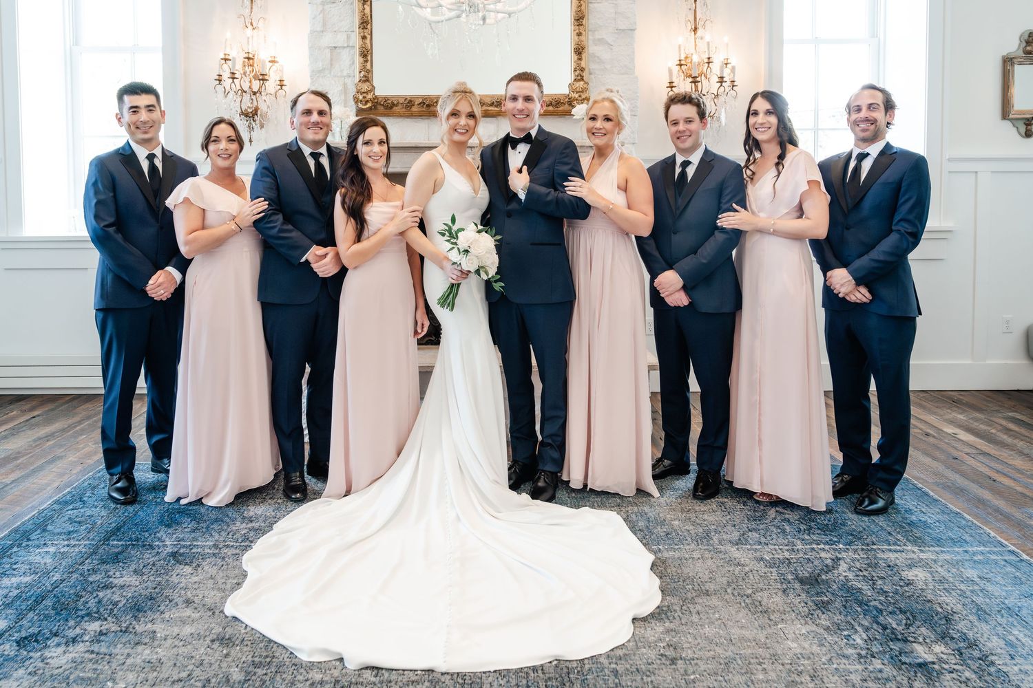 Wedding party in blush pink dresses and navy suits poses together on outdoor stone steps.