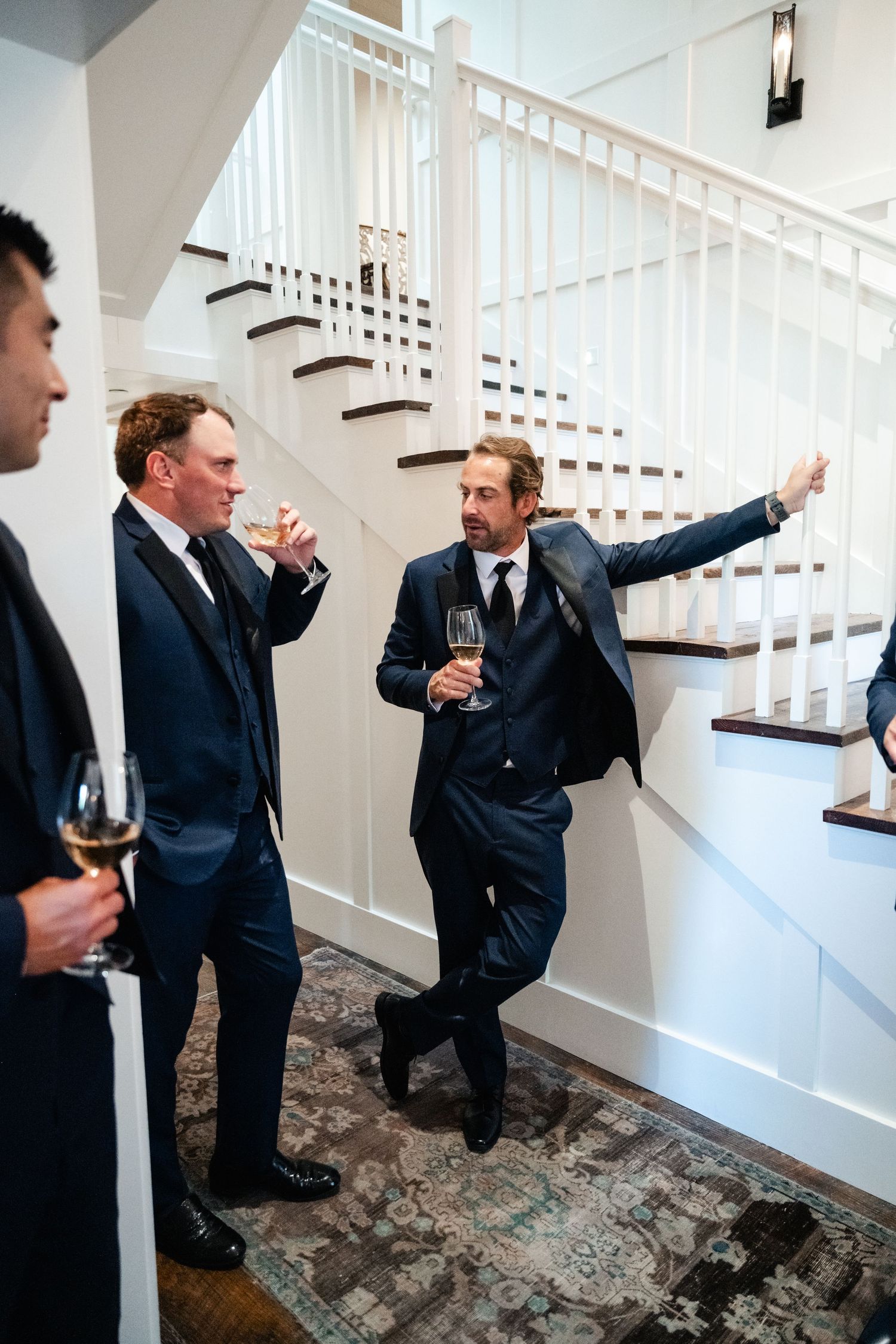 Groomsmen in dark suits pose playfully on carpeted stairs during wedding festivities.