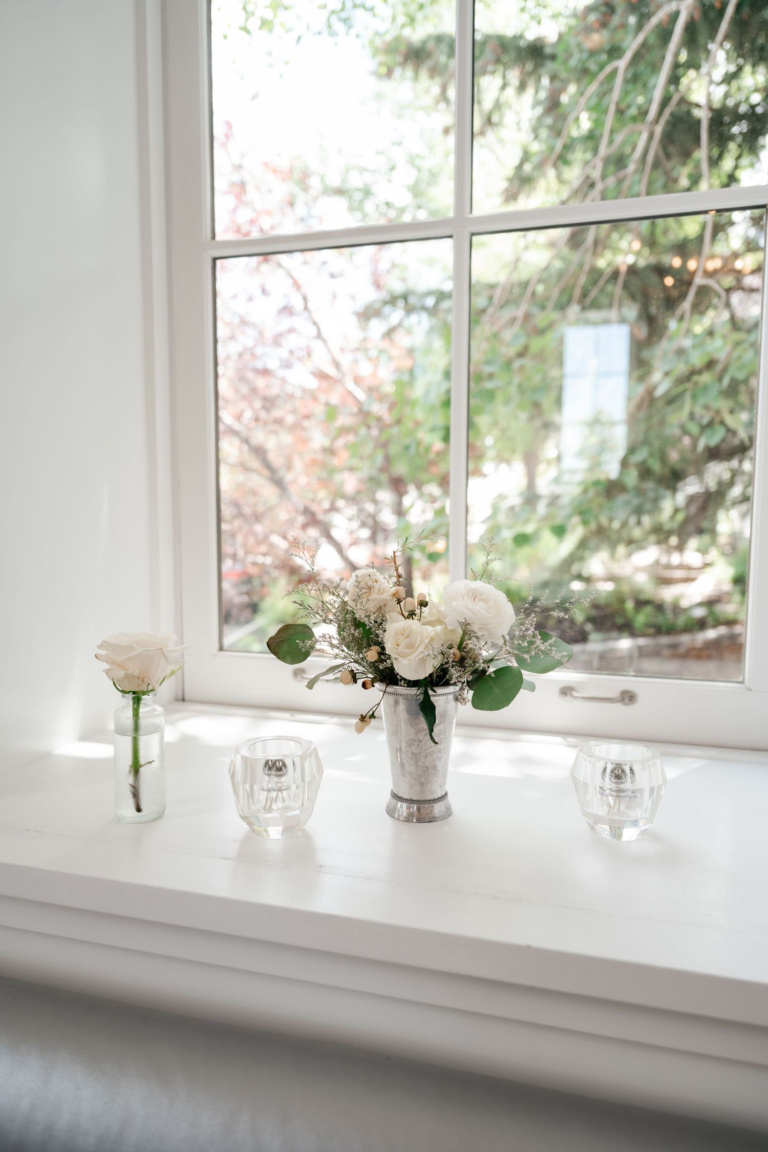 Delicate white floral arrangements in crystal vases line a bright windowsill with natural light streaming in.