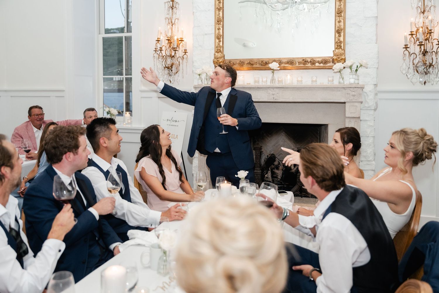 Wedding reception guests celebrate with raised glasses in an elegant white-walled venue.