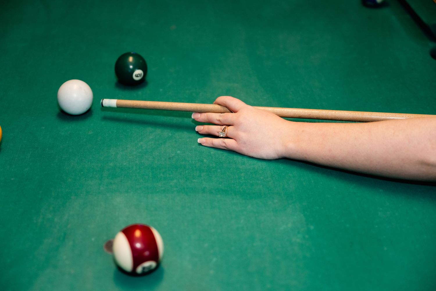 Close-up shot of a pool cue stick lining up to hit the white cue ball on a green felt table.