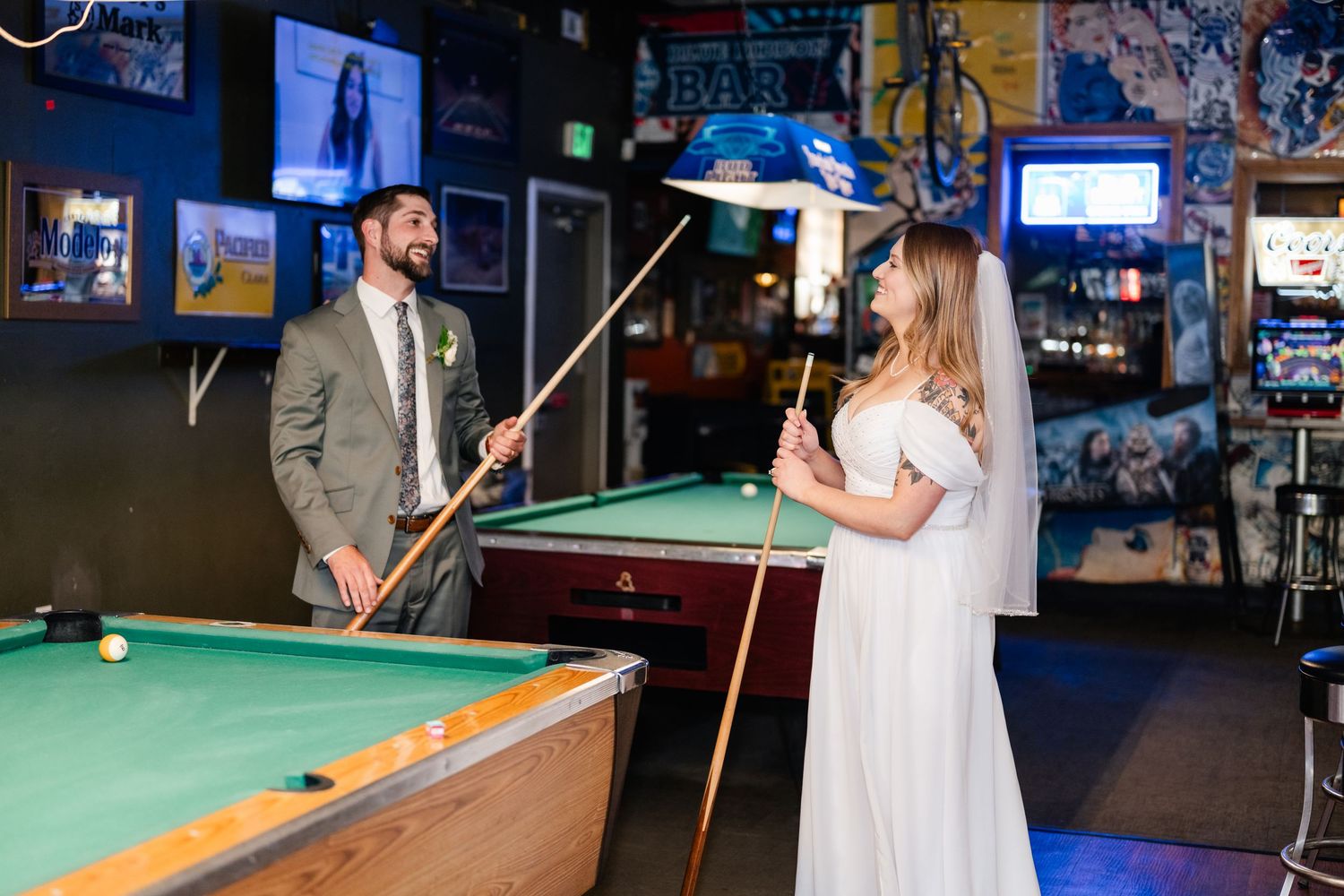 A couple plays pool together in wedding attire at a casual sports bar.