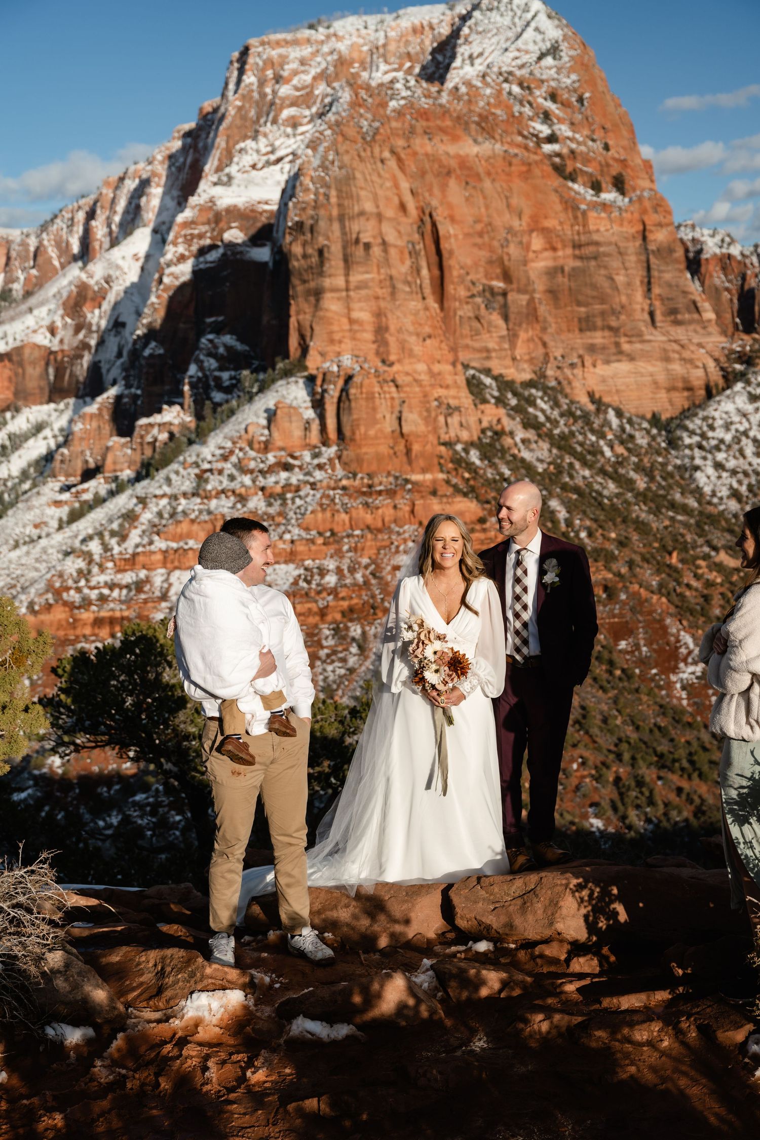 Newlyweds share an intimate moment with stunning red rock formations and snowy peaks in the background.