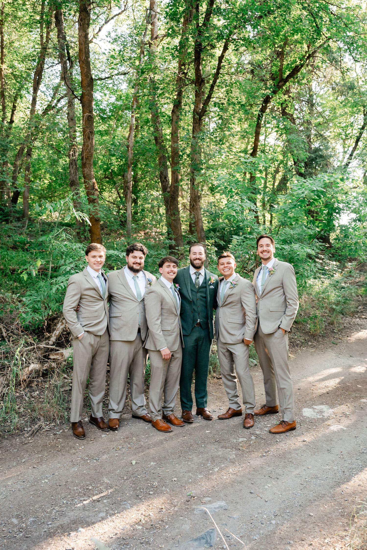 Wedding party in coordinated tan and navy suits posing on a wooded path. Utah Mountain Wedding.
