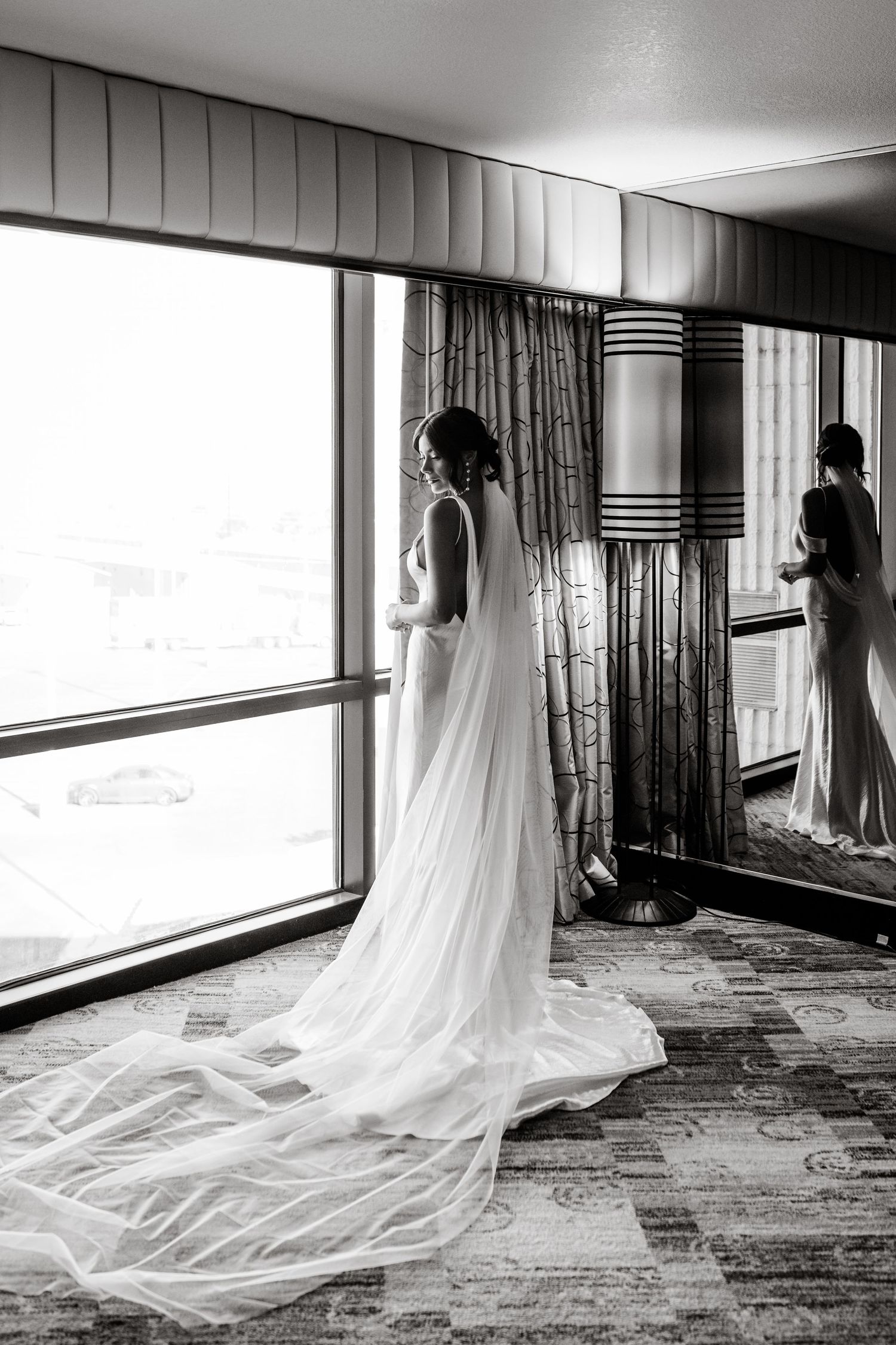 A flowing white wedding dress train creates an elegant silhouette against a carpeted floor in black and white.