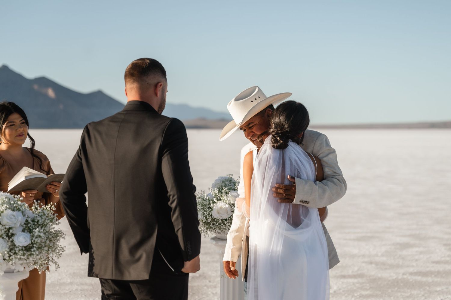 Wedding party gathering on vast salt flats with mountains in the distance.