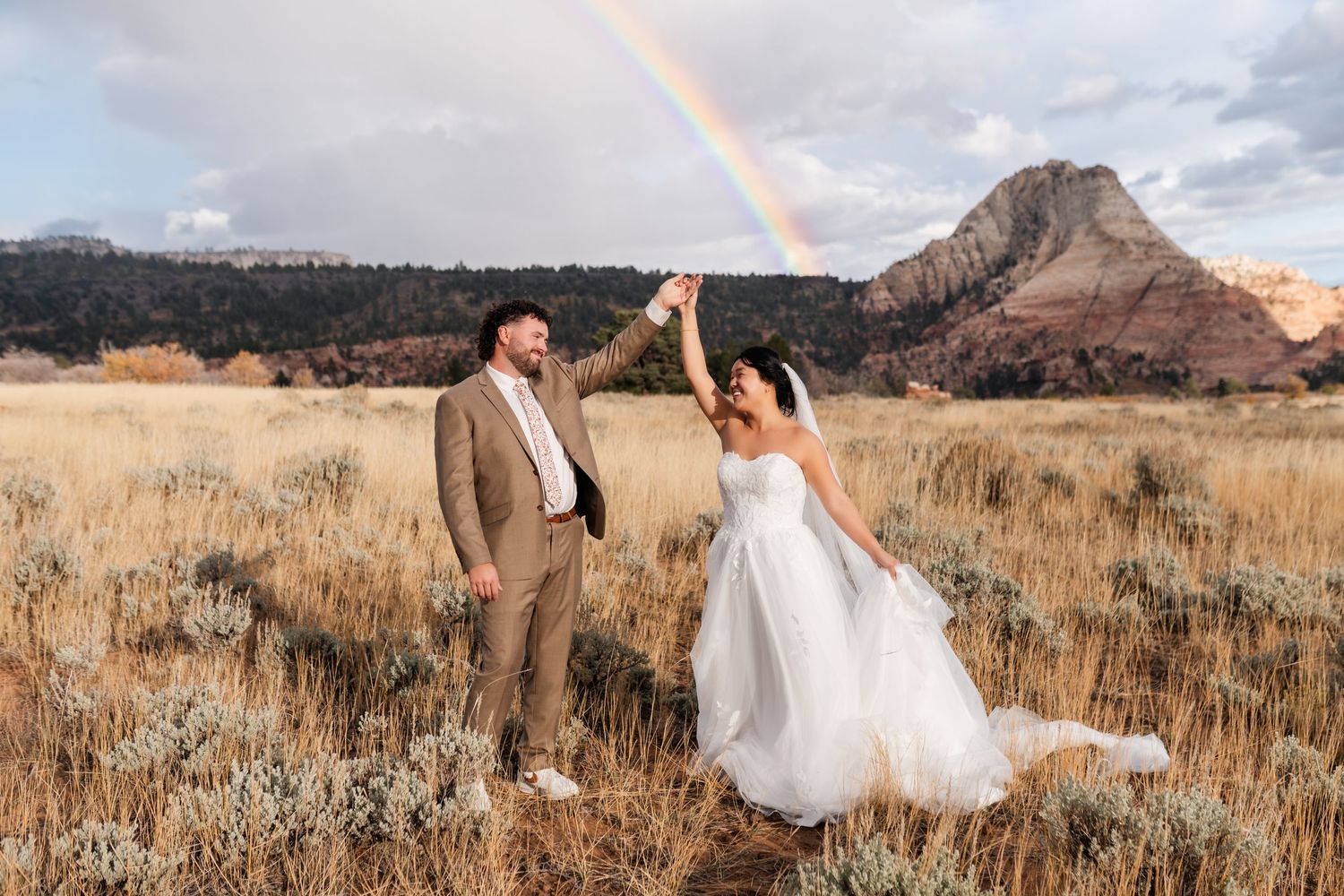 A couple in wedding attire poses romantically in a golden wheat field with mountains in the background at sunset. Zion Wedding Photographer.