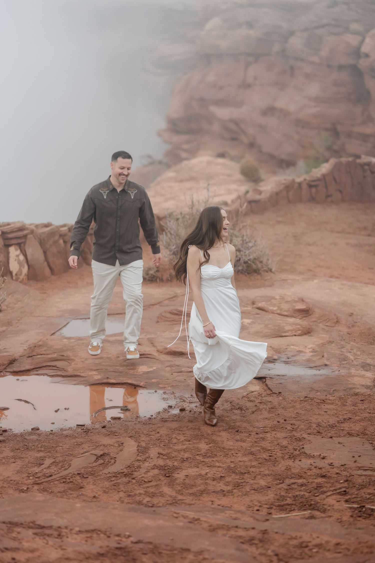 A couple walks together on red rock formations in a desert landscape during sunset.