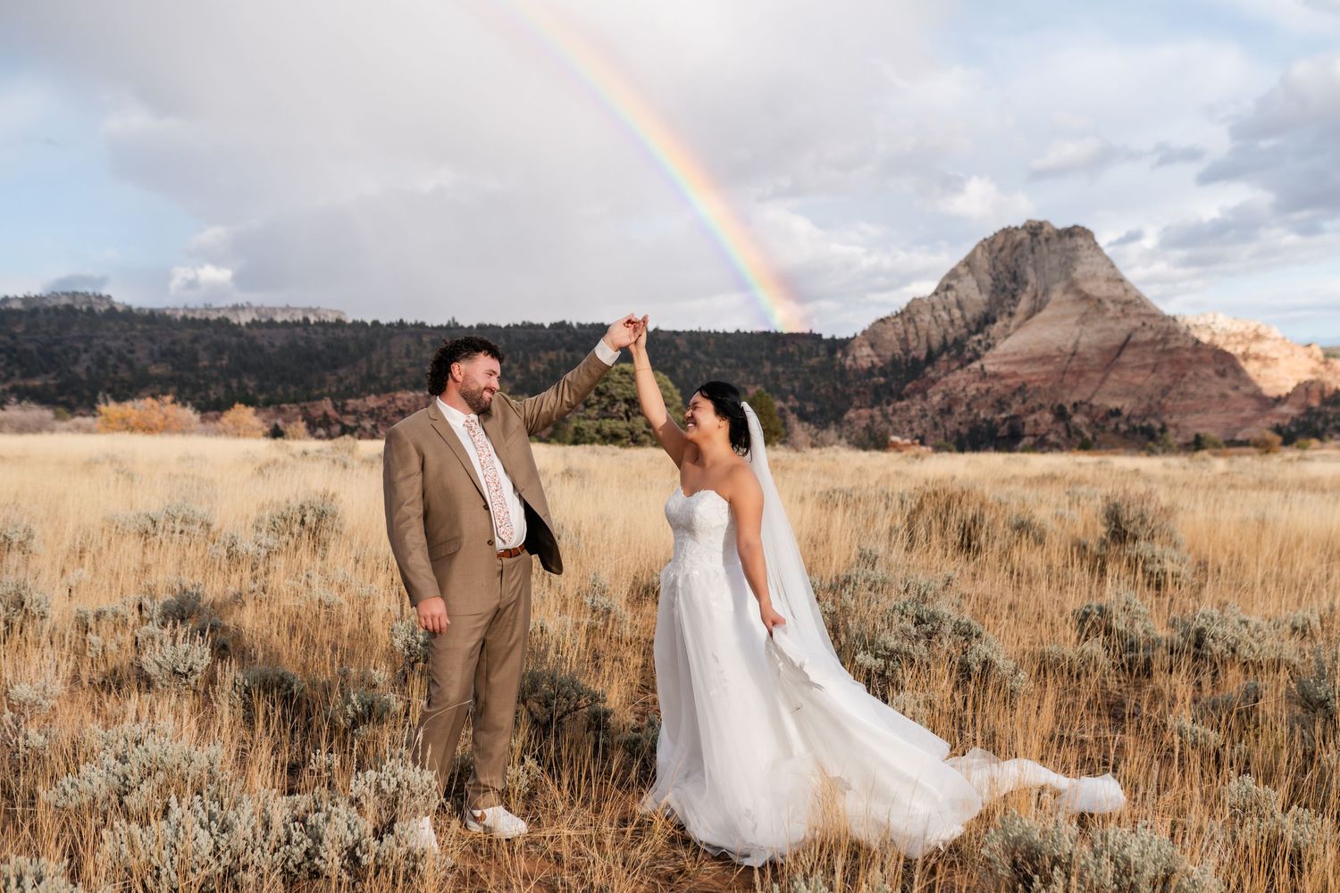 A couple in wedding attire embraces in a scenic mountain landscape at sunset.