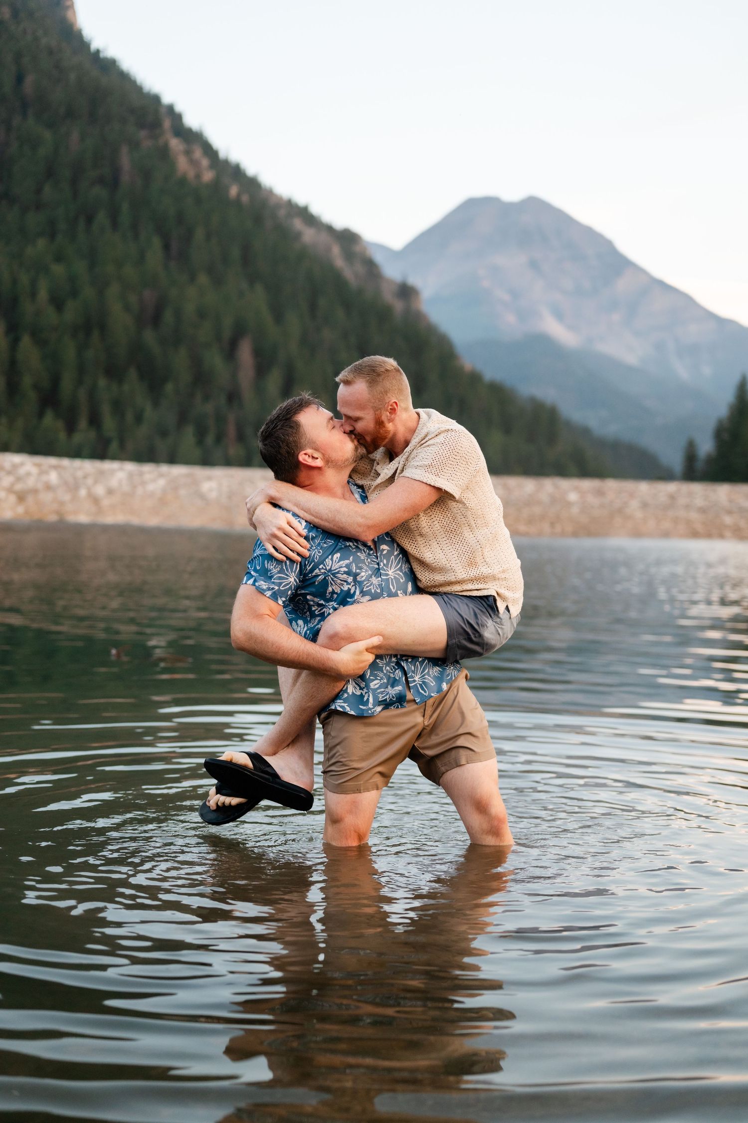 Couple having a water fight at Tibble Fork Reservoir. Two men embracing and laughing in a mountain lake with scenic peaks behind them.