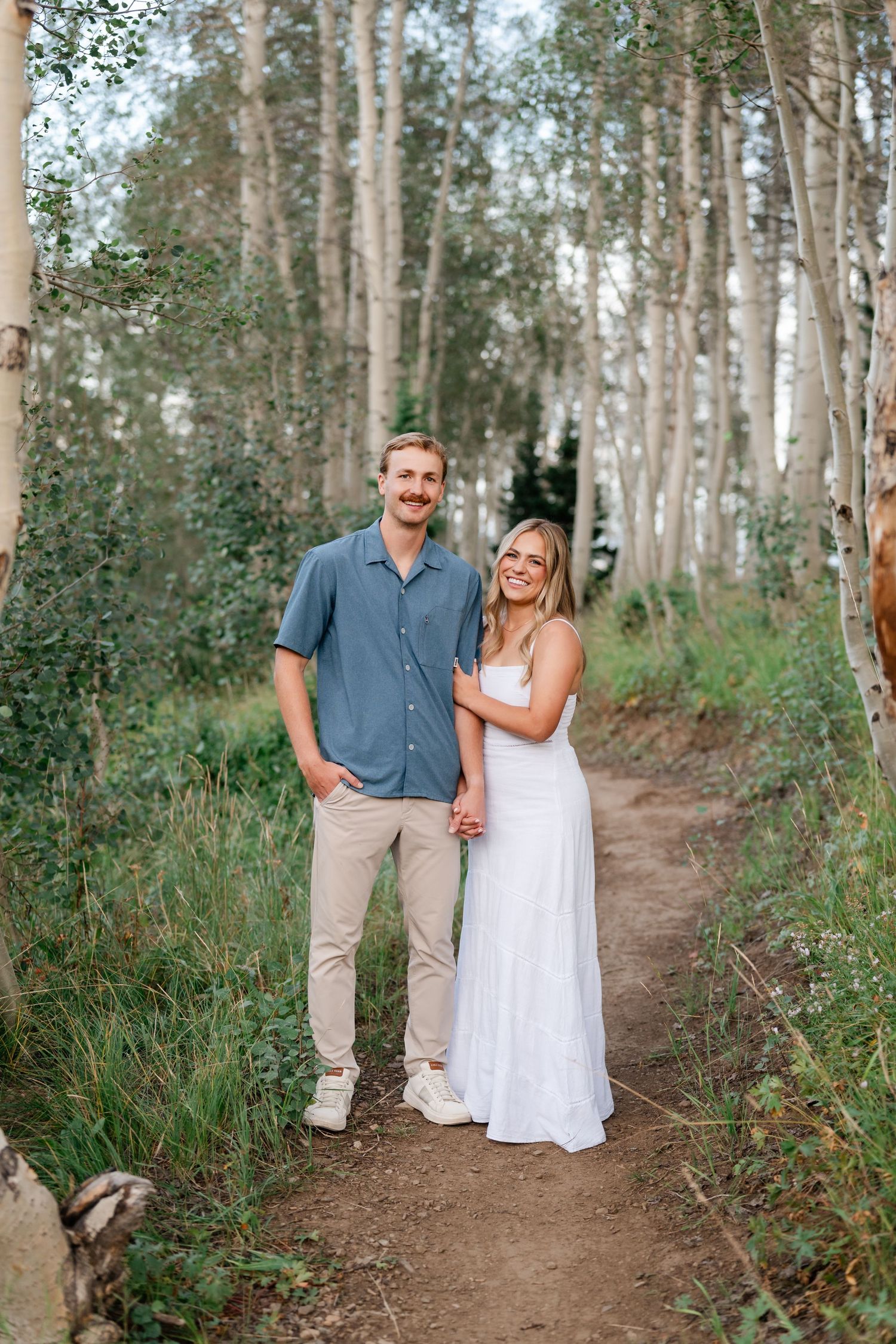 Couple holding hands on a forest path among aspen trees during mountain engagement photos near Deer Valley and Park City.