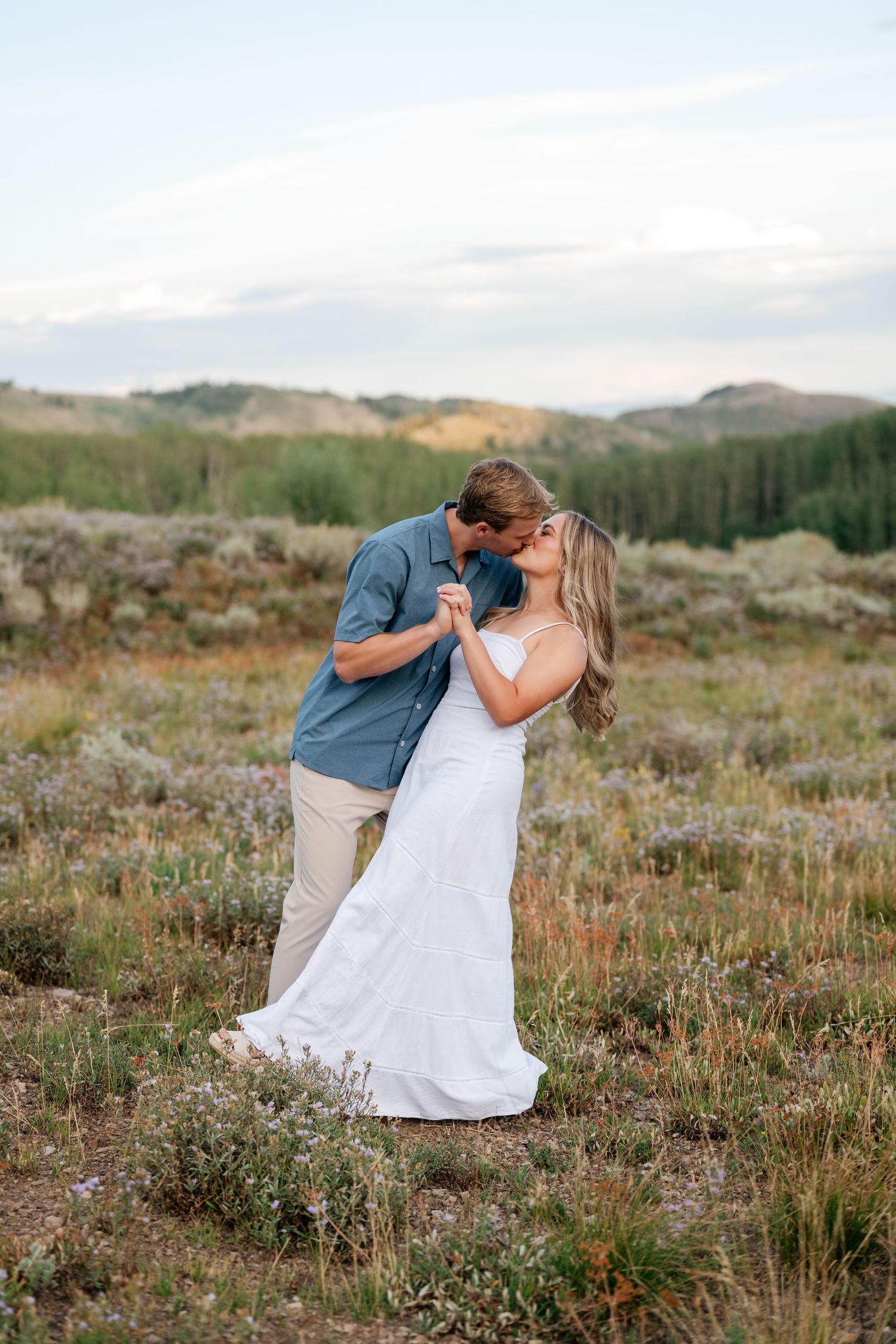 Park city mountain engagement photos at sunset. Couple sharing a romantic kiss in a wildflower meadow, mountains behind.