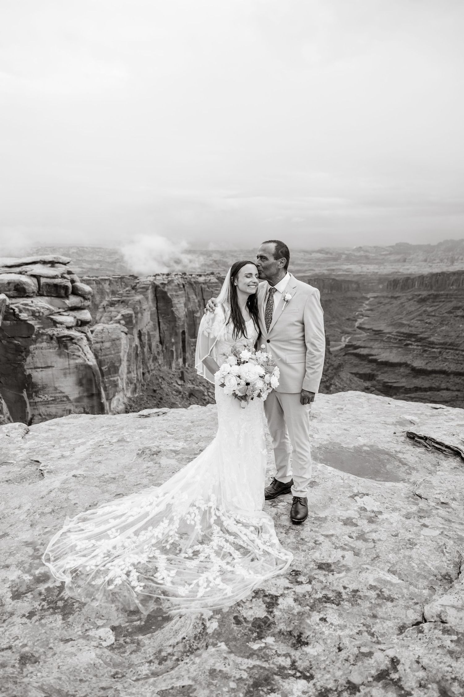 Black and white wedding portraits showcasing bride's dramatic train against canyon vista.