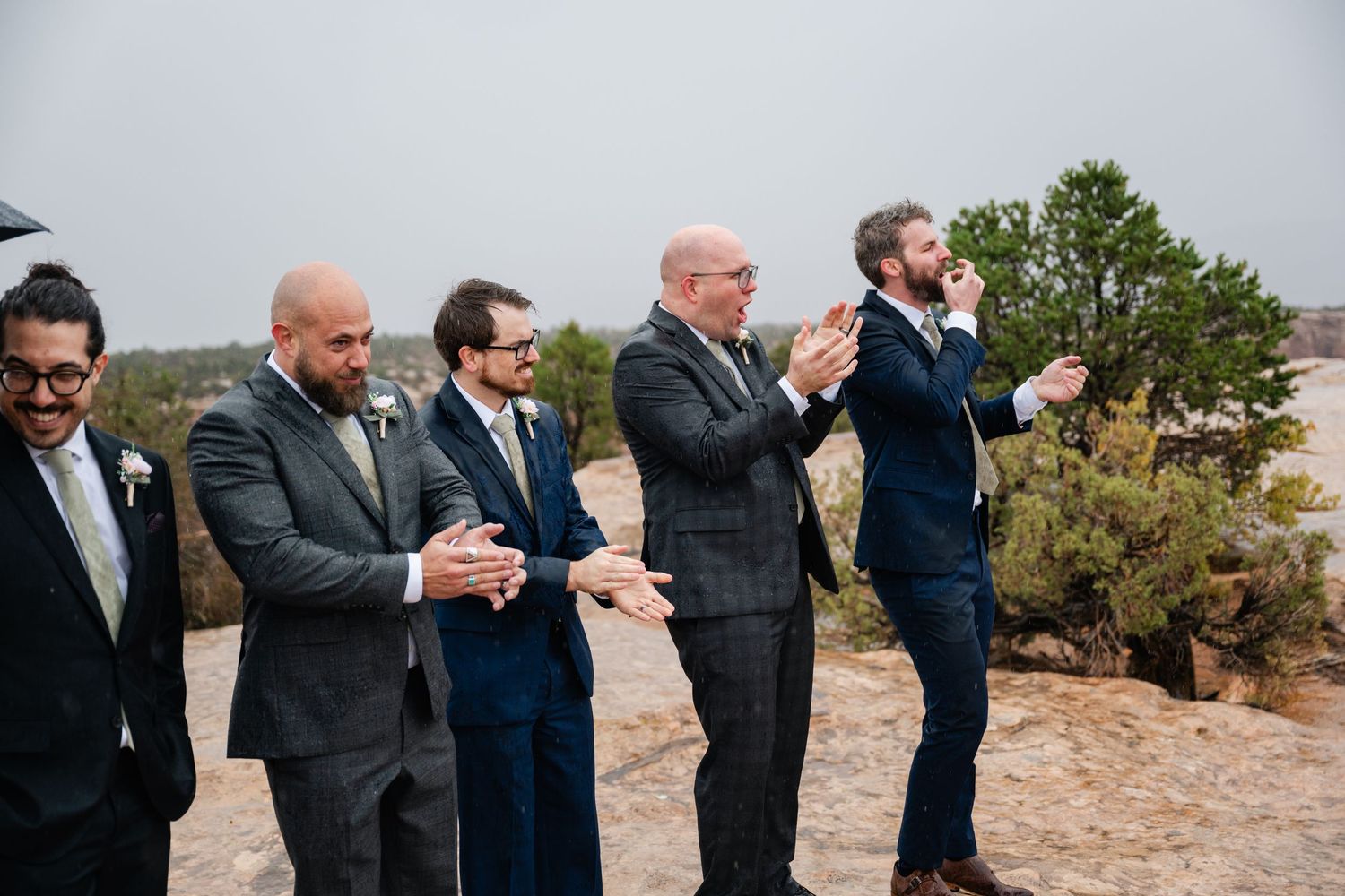 Groomsmen in formal attire react emotionally during outdoor ceremony.