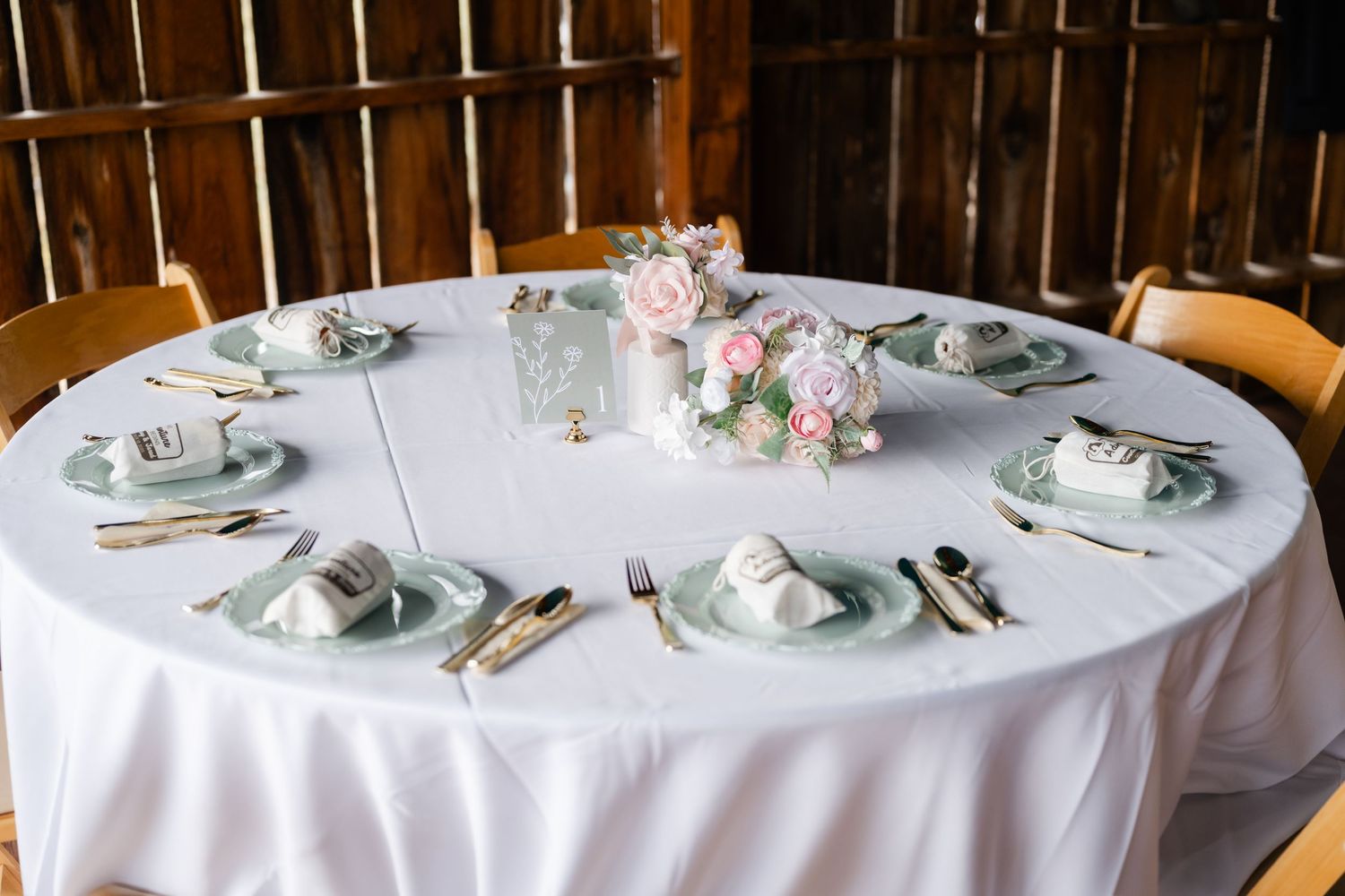 Round wedding reception table with white linens and place settings in rustic barn venue.