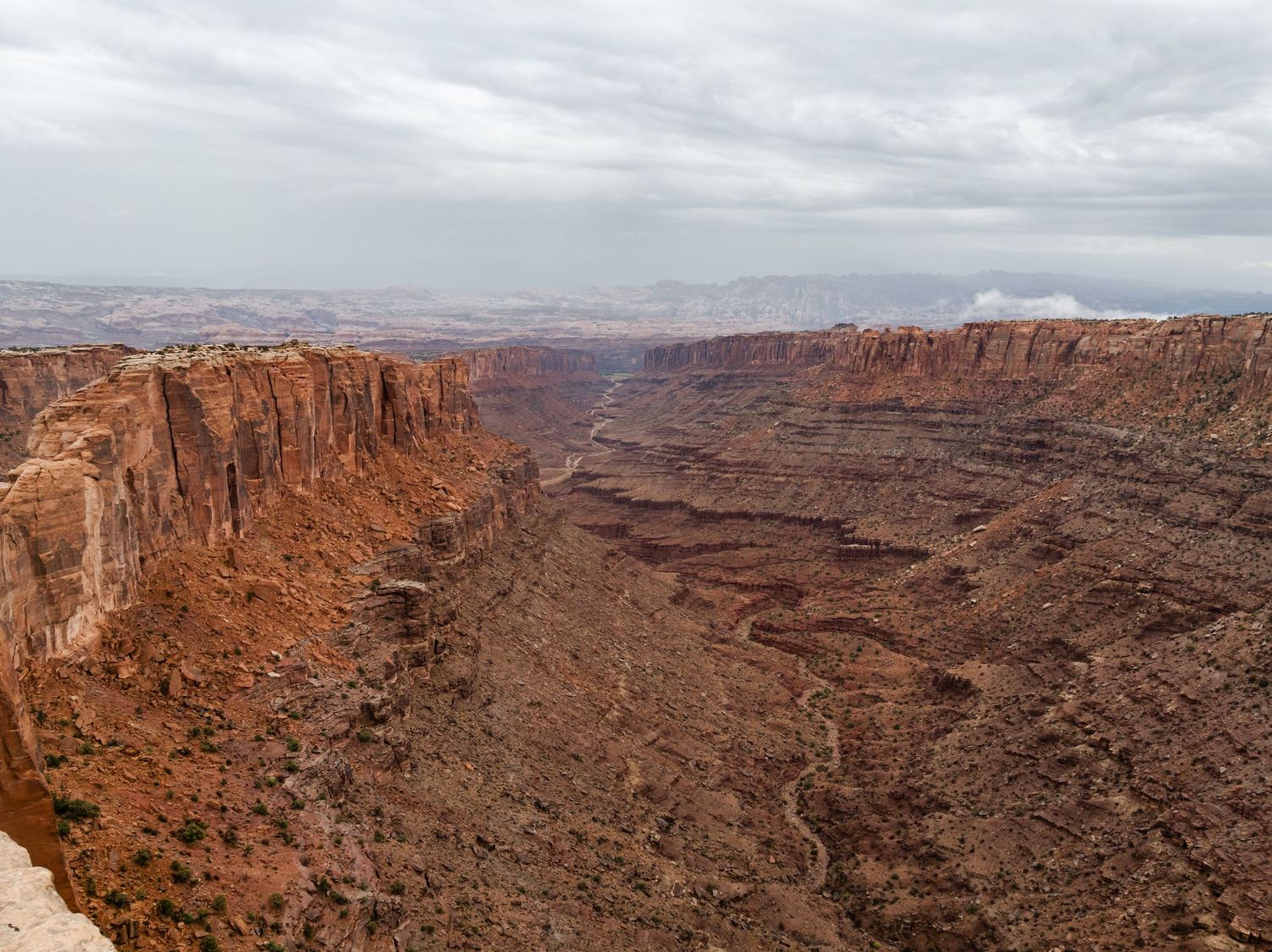 Dramatic aerial view of red rock canyons and cliffs in a desert landscape under cloudy skies.
