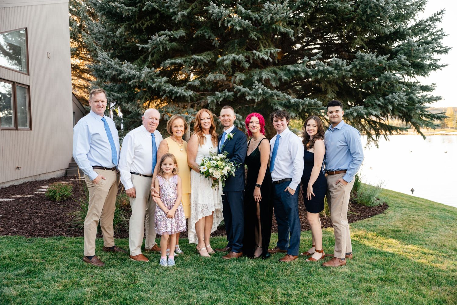 A group poses for a casual outdoor photo in front of evergreen trees.