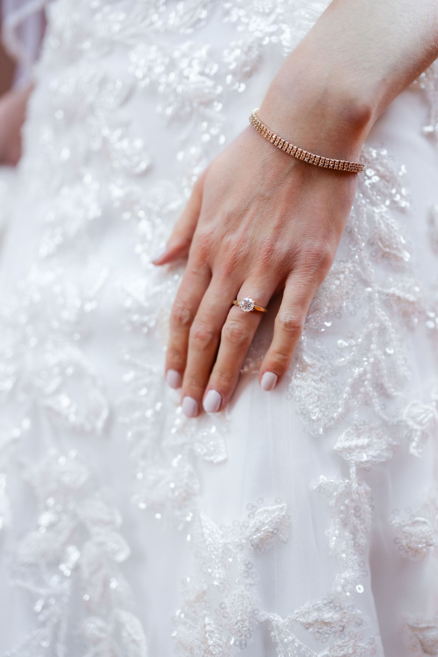 Close-up detail of a lace wedding dress with a delicate ring on the bride's hand.