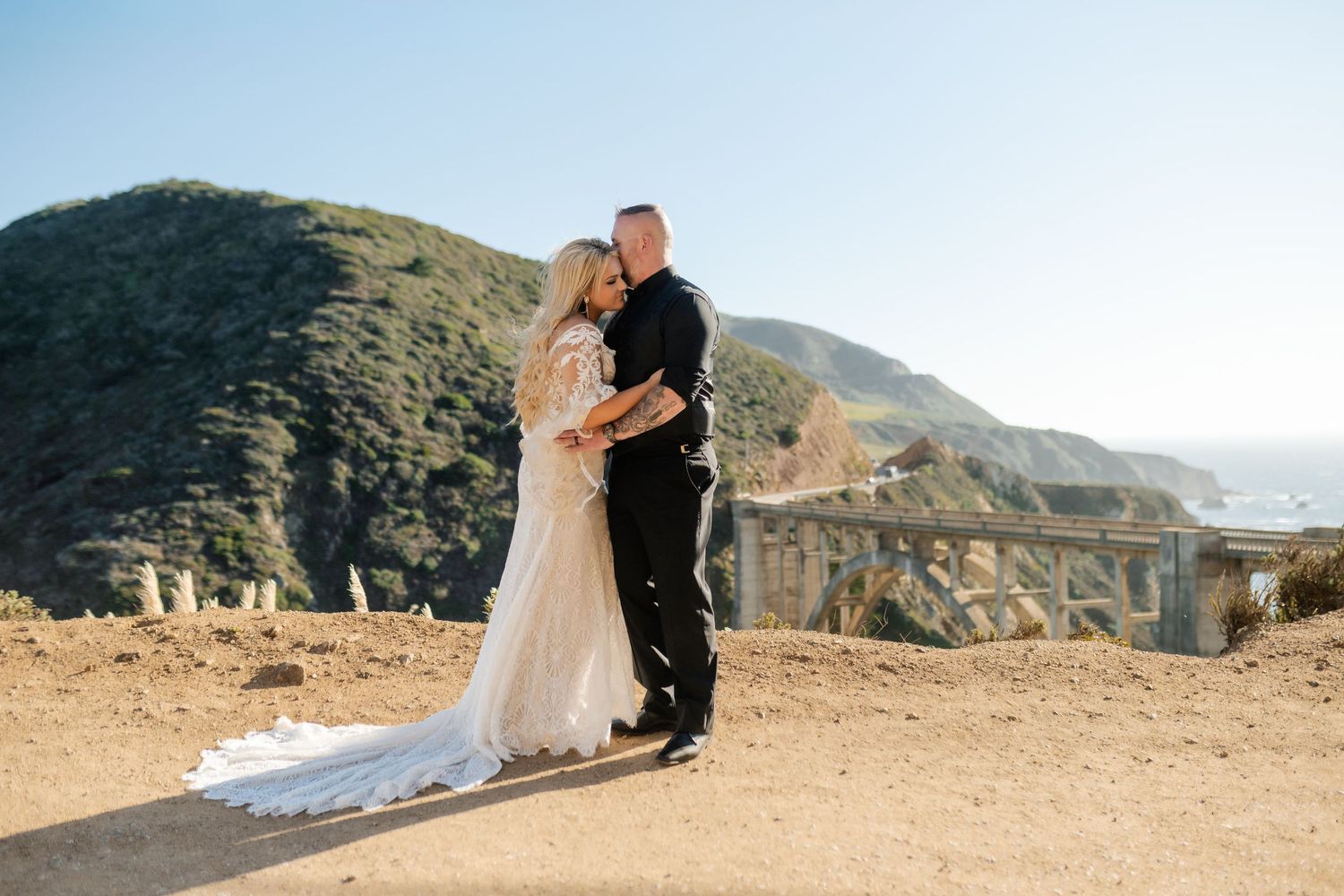 A couple shares an intimate moment on a scenic mountain overlook with dramatic coastal views.