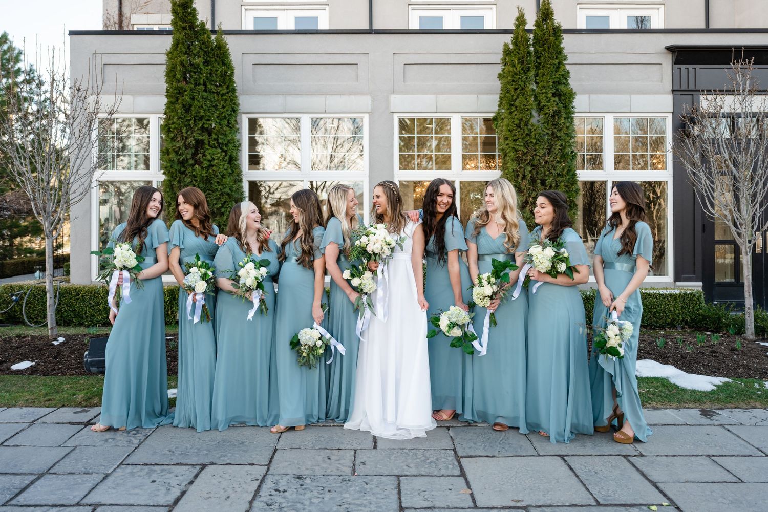 A wedding party in turquoise bridesmaid dresses poses together in a garden setting at Sleepy Ridge, a Utah County wedding venue.