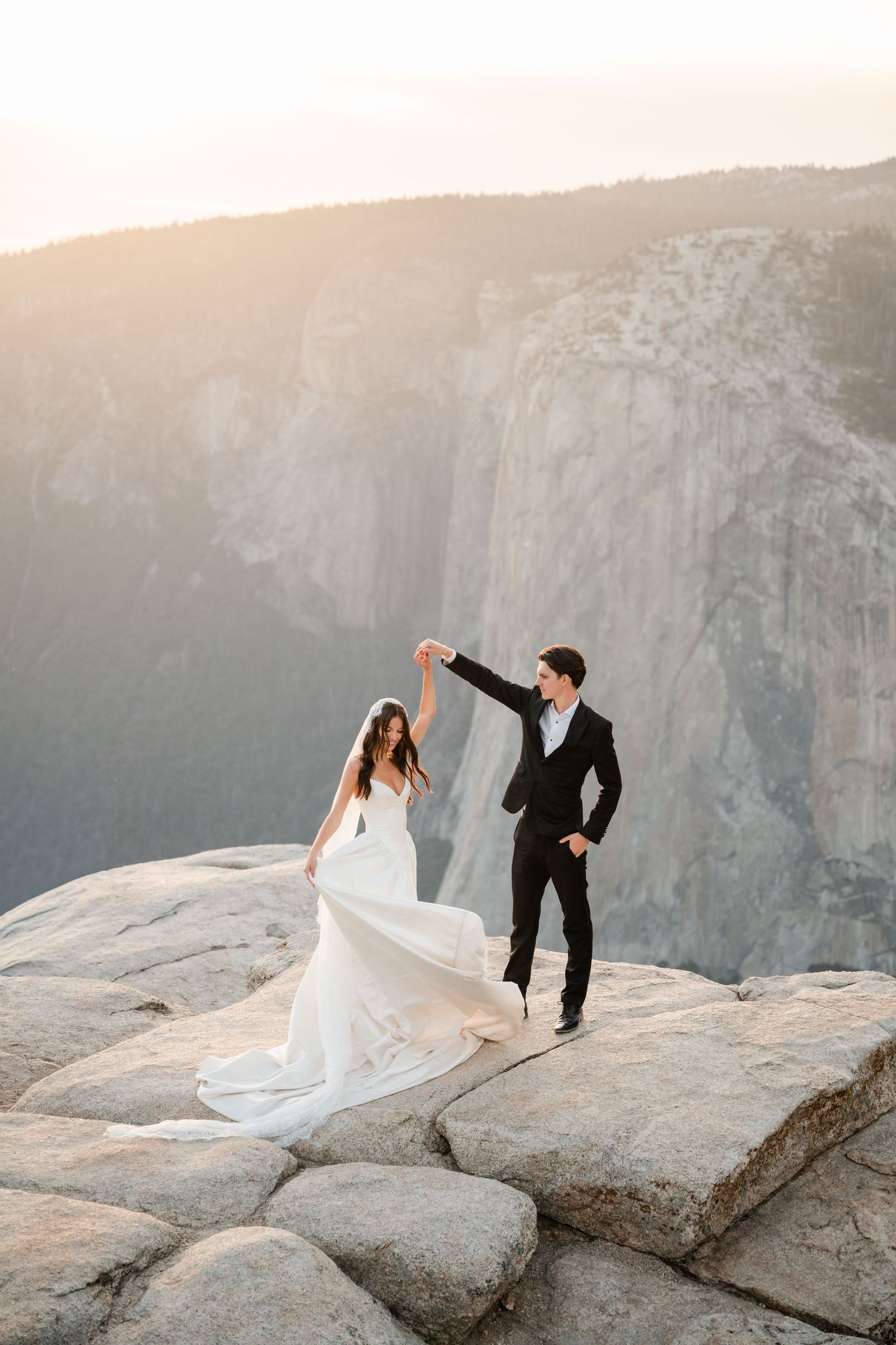 Bride and groom dancing on a rocky cliff at sunset with Yosemite valley views.