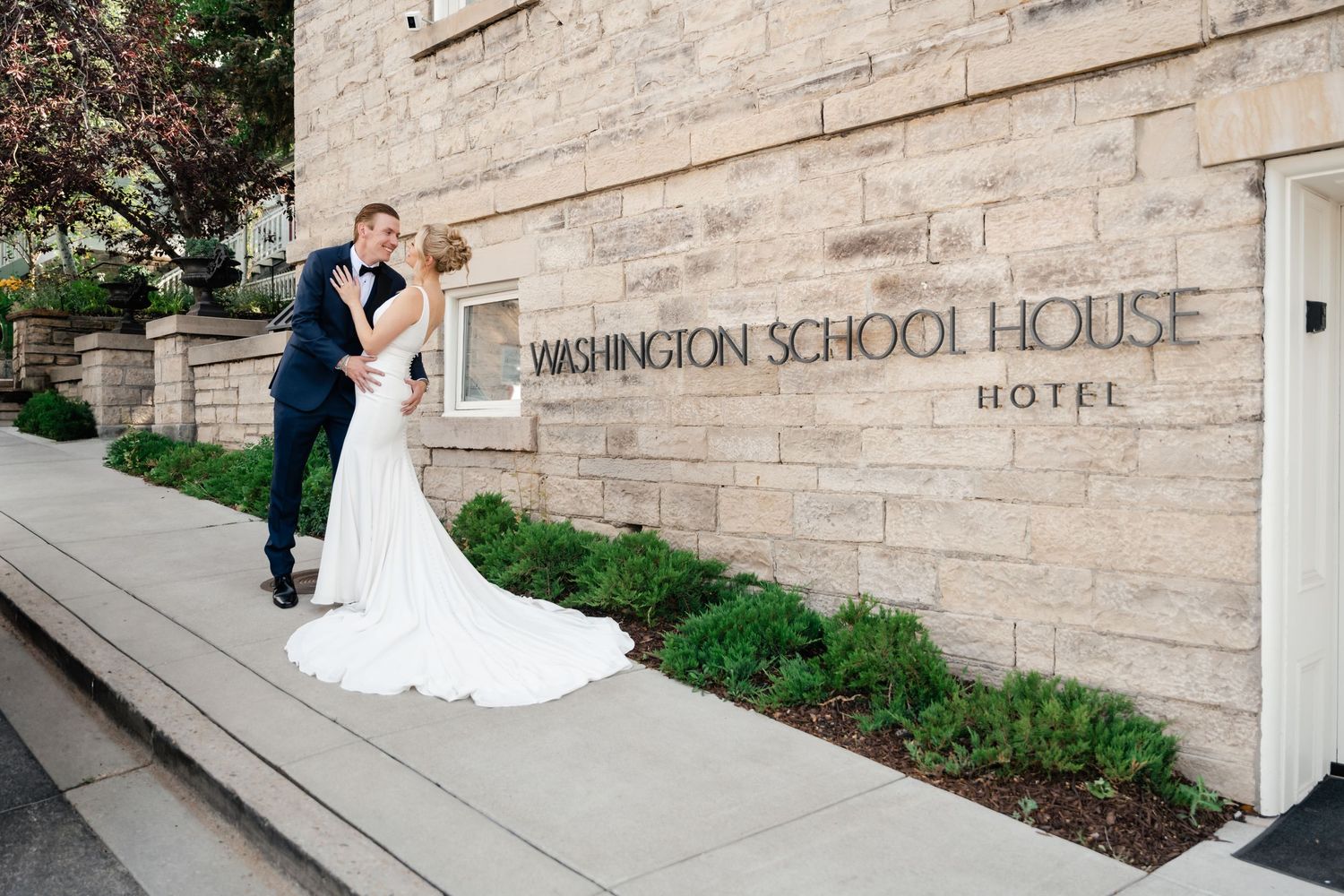 Bride and groom sharing a romantic kiss outside Washington School House Hotel on their wedding day.